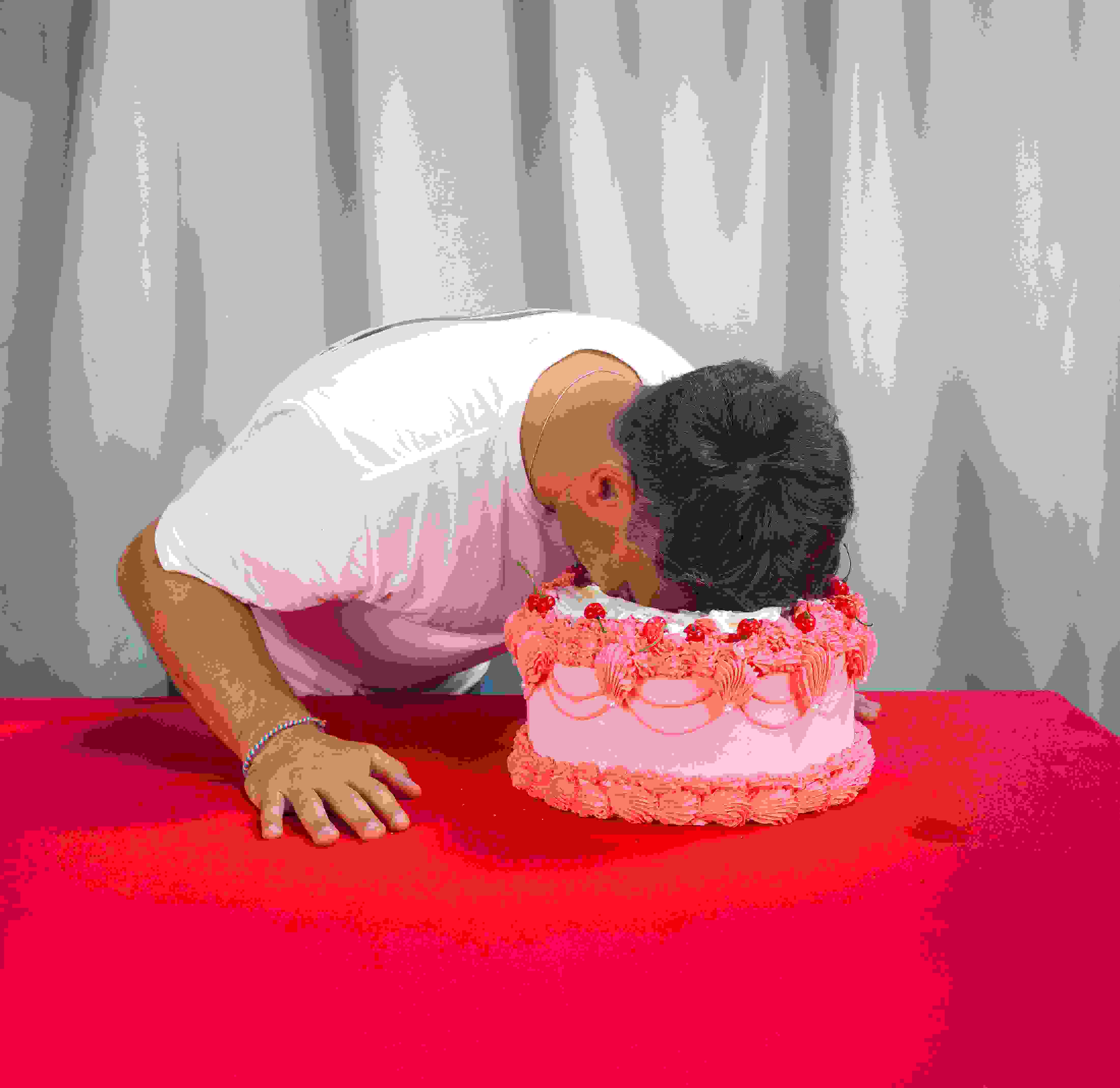 Daniel taucht Kopf in rosa Torte auf rotem Tisch. kreative Eventidee, außergewöhnliche Eventfotografie, spass, humor, Markenerlebnis, Brand Experience, Eventplanung, Publicevent, Eventagentur Bern, Technik, Beleuchtung, Live Kommunikation, networking anlass, Mitarbeiteranlass, Mitarbeiter:innen-anlass, Jubiläumsfeier, Weihnachstfeier firma, Party, networking anlass, Corporate-Event