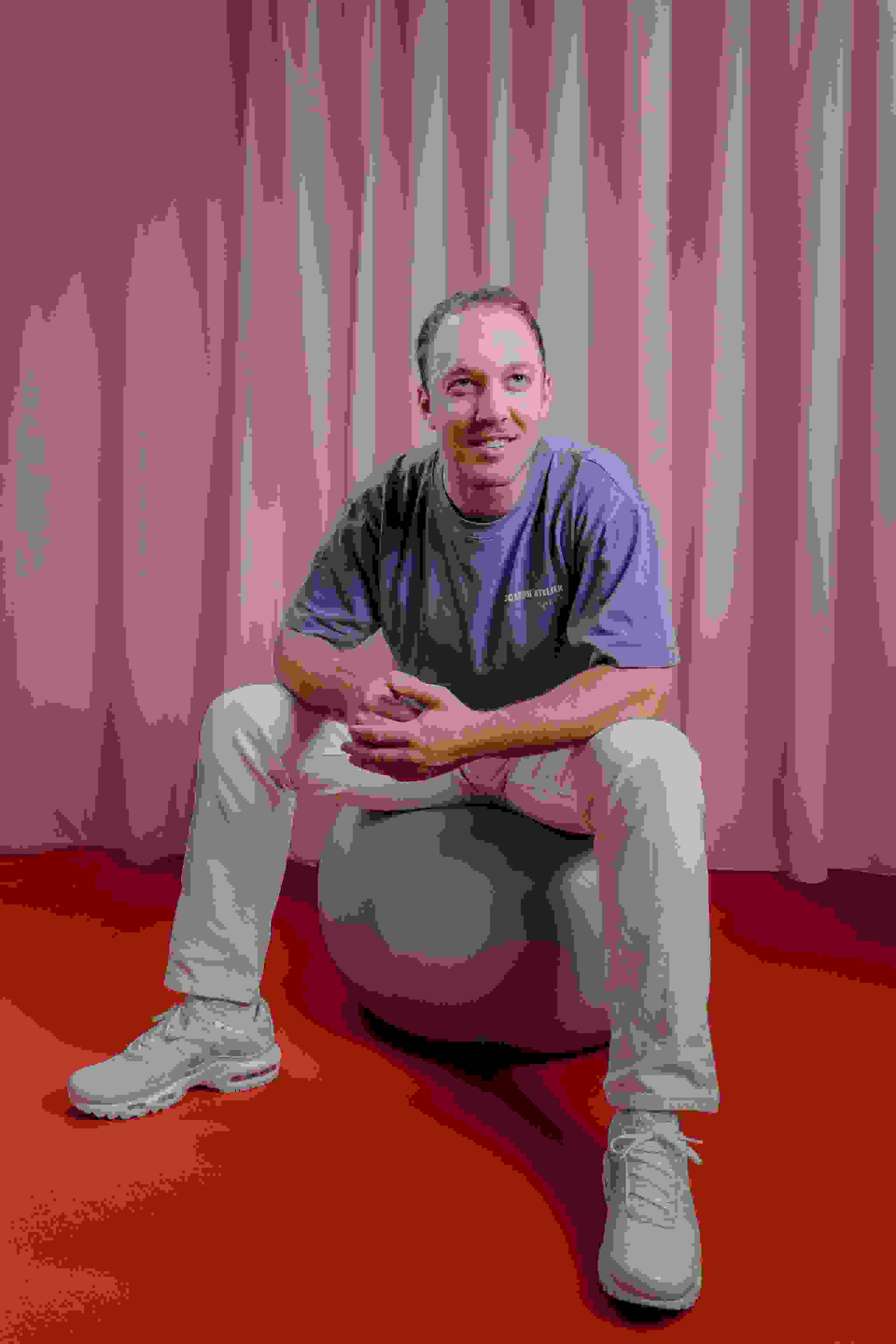Mitarbeiter Thierry Riedo der Live Kommunikations Agentur evenjo auf einem Gymnastikball vor rosa Vorhang. live kommunikation, Corporate-Event, Eventagentur bern, eventplanung, firmenevents, teamevents bern, jubiläumsfeier, networking anlass, mitarbeiteranlass, evenjo-Team, Technik, Junior Projektleitung, Beratung