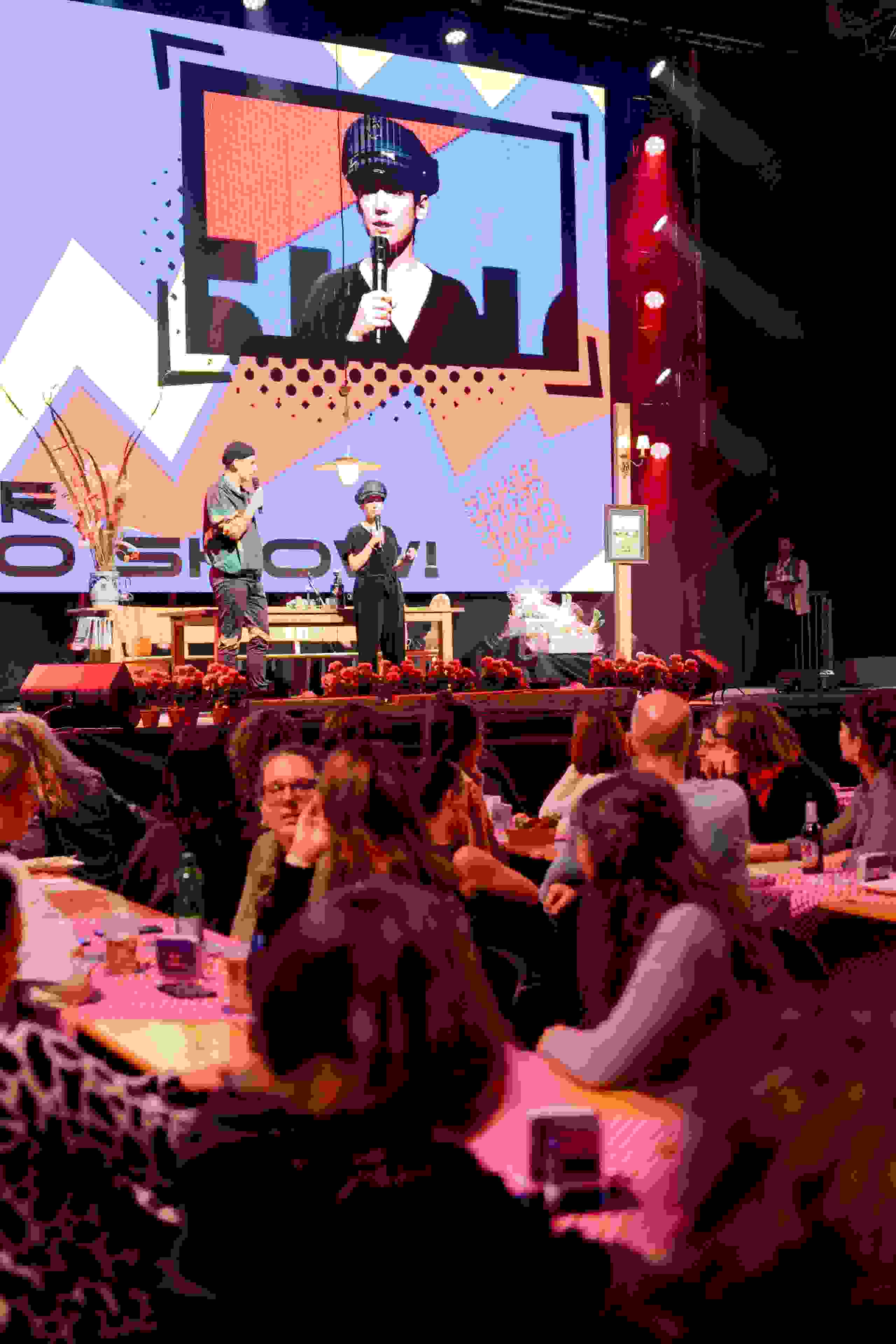 Zwei Moderatoren auf der Bühne vor kreativem Bühnenbild – unterhaltsames Programm für ein grosses, aktives Publikum. Live-Show, Moderation, Supermercado, Publikumsinteraktion, Kulturprogramm, eventagentur bern, Eventtechnik, live kommunikation, markenerlebnis, Lotto, Gülsha Adilji, 