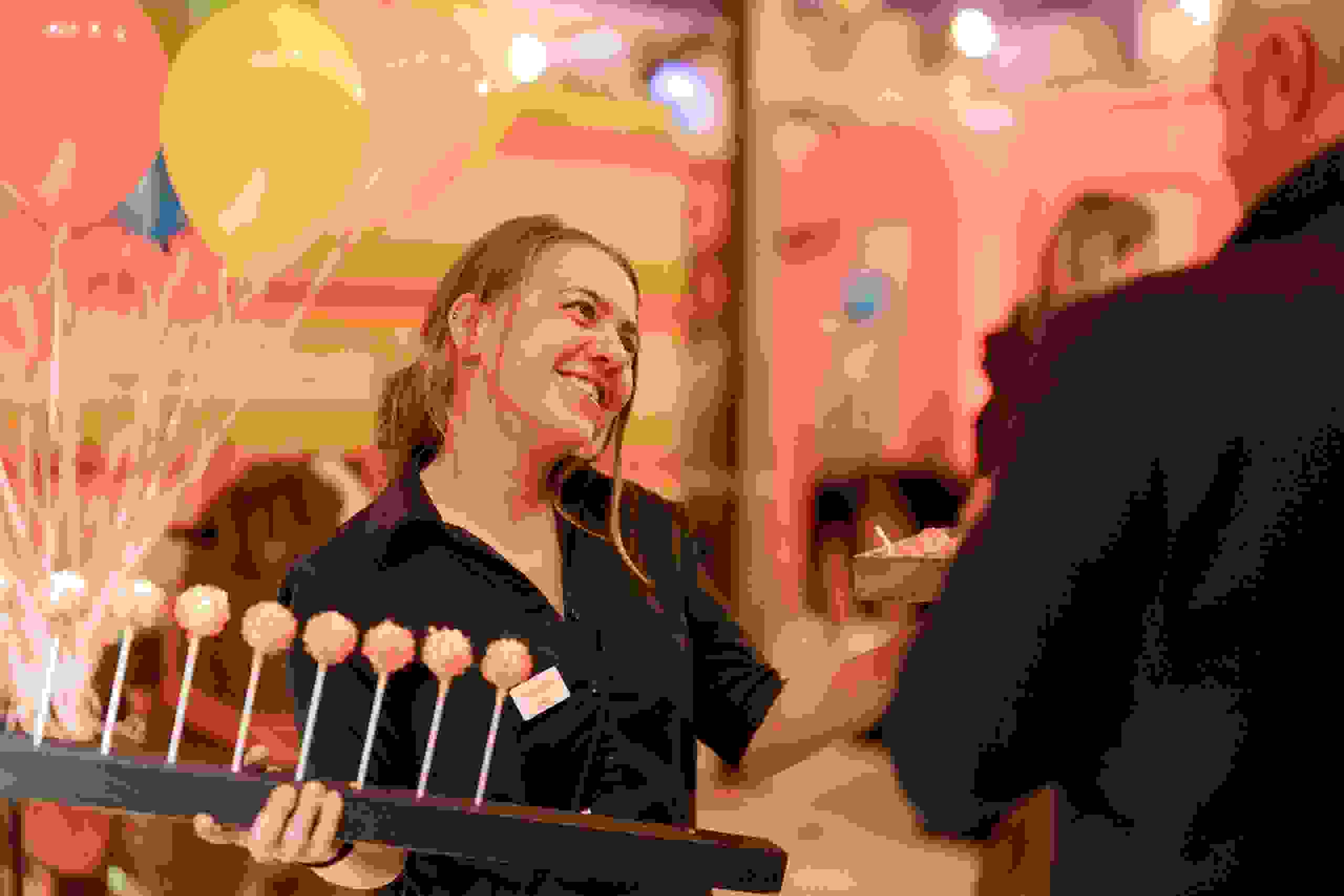 Lachende Servicekraft mit Cake Pops im Gespräch bei der evenjo Sause. Begegnung, Networking, Live-Kommunikation, Eventgestaltung, Markenerlebnis, Brand Experience, Eventplanung, Publicevent, Eventagentur Bern, Corporate-Event, Mitarbeiteranlass, Mitarbeiter:innen-Anlass, Live Kommunikation, networking Anlass