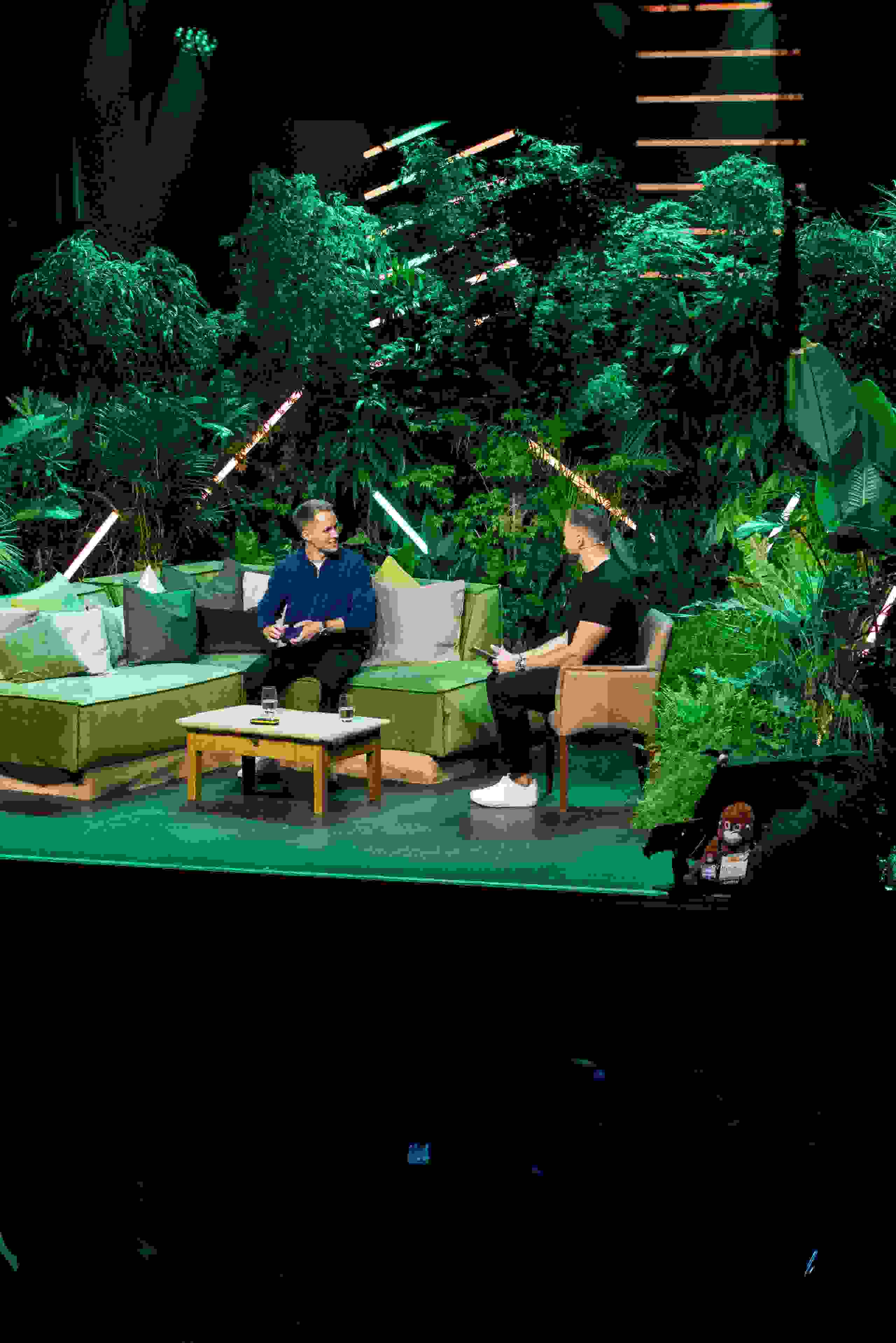 Zwei Männer im Gespräch auf grüner Dschungel-Bühne beim Unfold 2024 – Podiumsdiskussion, Eventinszenierung, Business-Event in Bern. Corporate Event, Eventbühne, Eventdesign, grüne Lichtstimmung, Dschungel Deko, Business Event, live kommunikation, Eventagentur bern, eventplanung, firmenevents, teamevents bern, jubiläumsfeier, networking anlass, mitarbeiter:innenanlass, Technik, Public Events, Sport und Entertainment Events, markenerlebnis, Brand Experience