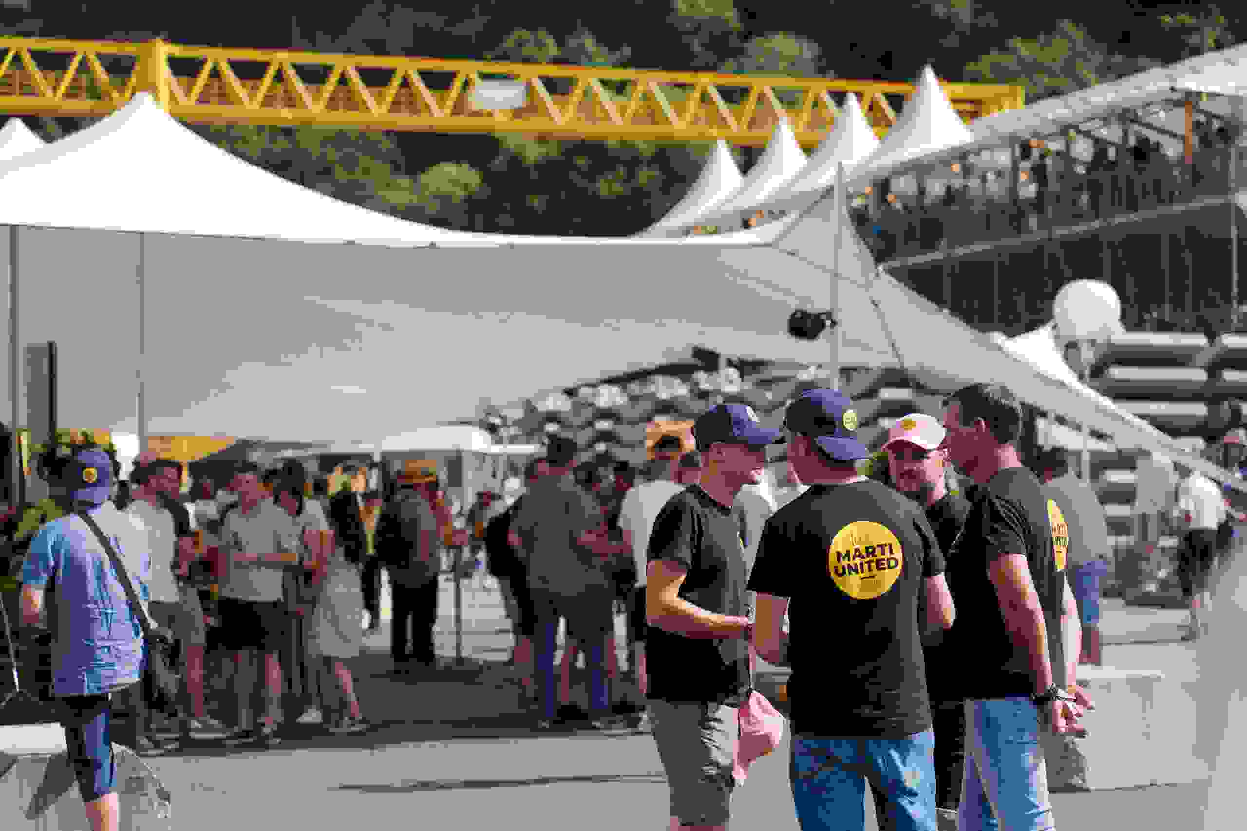 Besucherinnen und Besucher beim Marti United 100 Jubiläumsfest unter und vor weissem Zelt. Networking, Live-Kommunikation, Firmenjubiläum Markenerlebnis, Brand Experience, Mitarbeiteranlass, Live Kommunikation, Corporate-Event, eventplanung, Jubiläumsfeier, Mitarbeiteranlass, Teamevent, 100 Jahre Marti AG, Festival