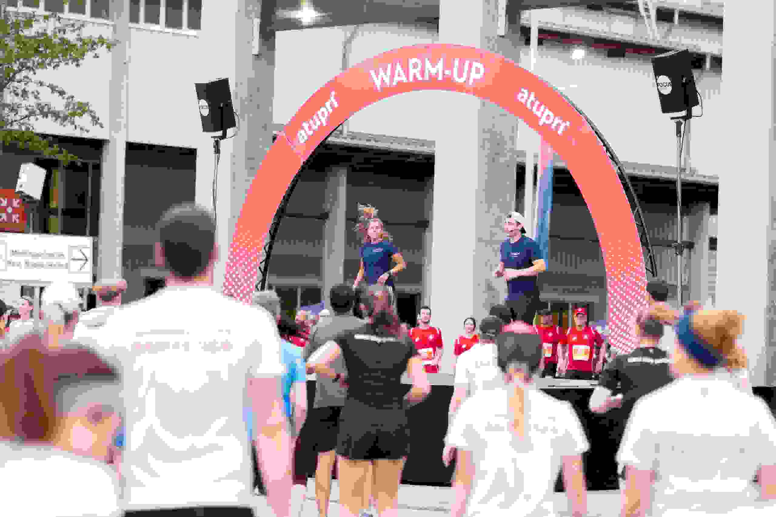 ufwärmtraining vor grosser Teilnehmergruppe unter dem Atupri Healthbox WARM-UP Bogen bei Sportevent. Atupri Healthbox, Warm-up, Gruppenfitness, Outdoor-Event, Gesundheitsförderung, Teamwork, live kommunikation, Corporate-Event, Eventagentur bern, eventplanung, firmenevents, teamevents bern, jubiläumsfeier, networking anlass, mitarbeiteranlass, Technik, Public Events, Sport und Entertainment Events, markenerlebnis, Brand Experience