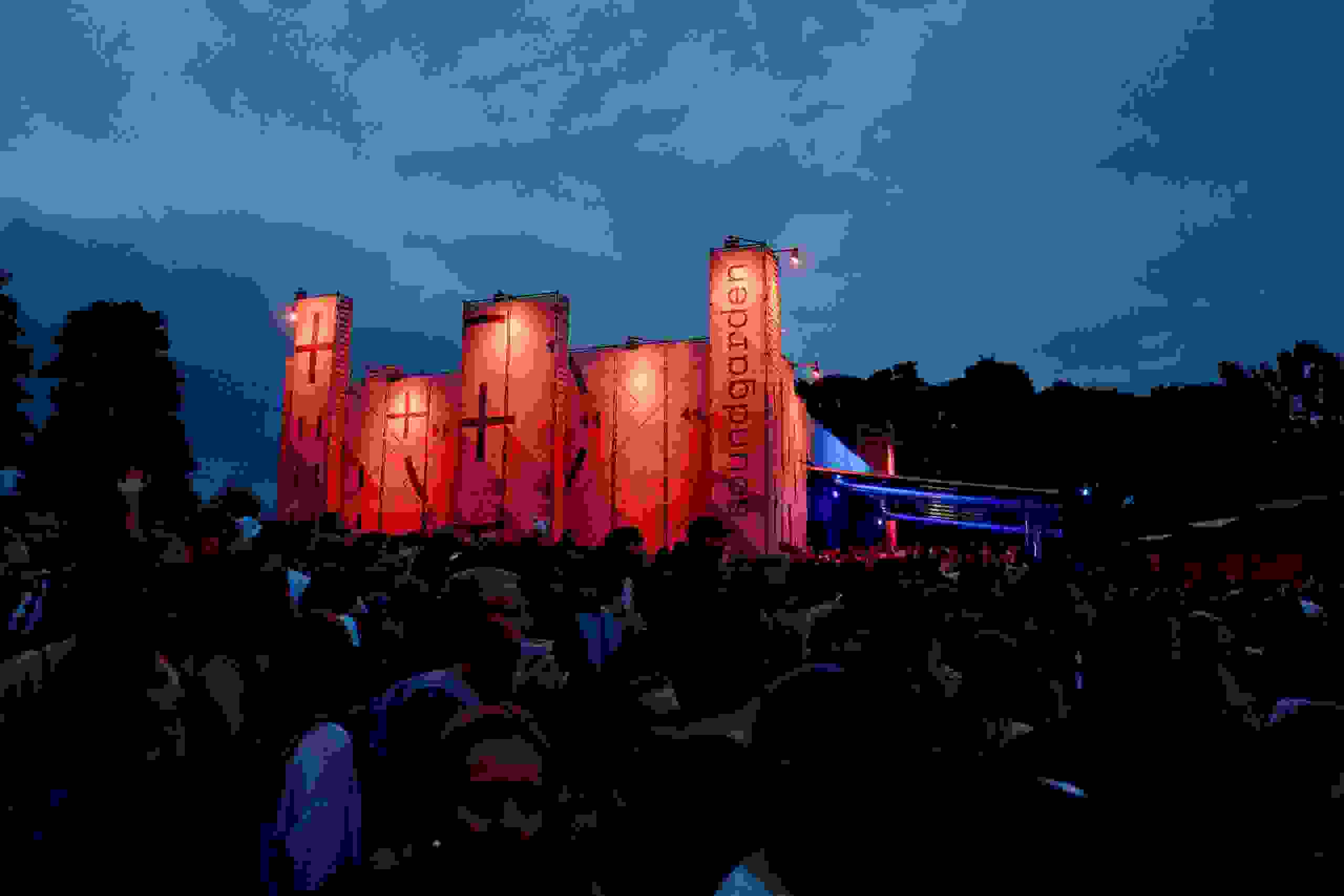 Der Soundgarden beim Gurtenfestival erstrahlt nachts in beeindruckendem rot mit Feuersäulen – spektakuläre Lichtinszenierung in Bern. Lichtshow, Nachtaufnahme, Bühne, Eventbeleuchtung, Festivalstimmung, Markenerlebnis, Brand Experience, Corporate-Event, eventplanung, Publicevent, Eventagentur Bern, Technik, Beleuchtung, Live Kommunikation, Gurten, Dancetents, Supermercado, cosmodrome