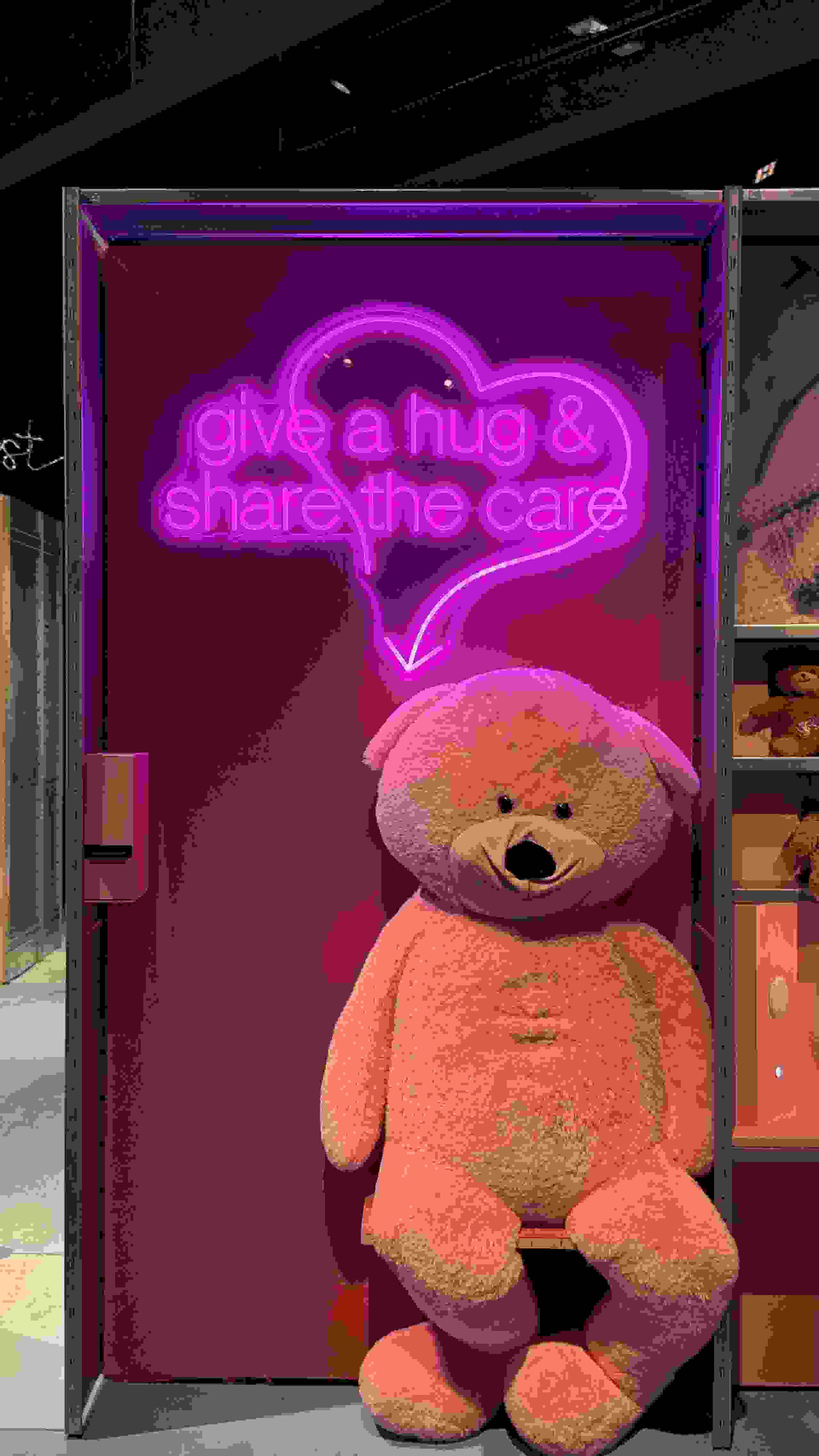 Ausstellungsraum im Stapferhaus mit riesen Teddybär und pinker Neon-Leuchtschrift "give a hug & share the care". moderne Szenografie. Ausstellungsgestaltung, Inszenierung, Begegnung, Networking, Live-Kommunikation, Eventgestaltung, Markenerlebnis, Brand Experience, Eventplanung, Publicevent, Eventagentur Bern, Corporate-Event, Mitarbeiteranlass, Mitarbeiter:innen-Anlass, Live Kommunikation, networking Anlass