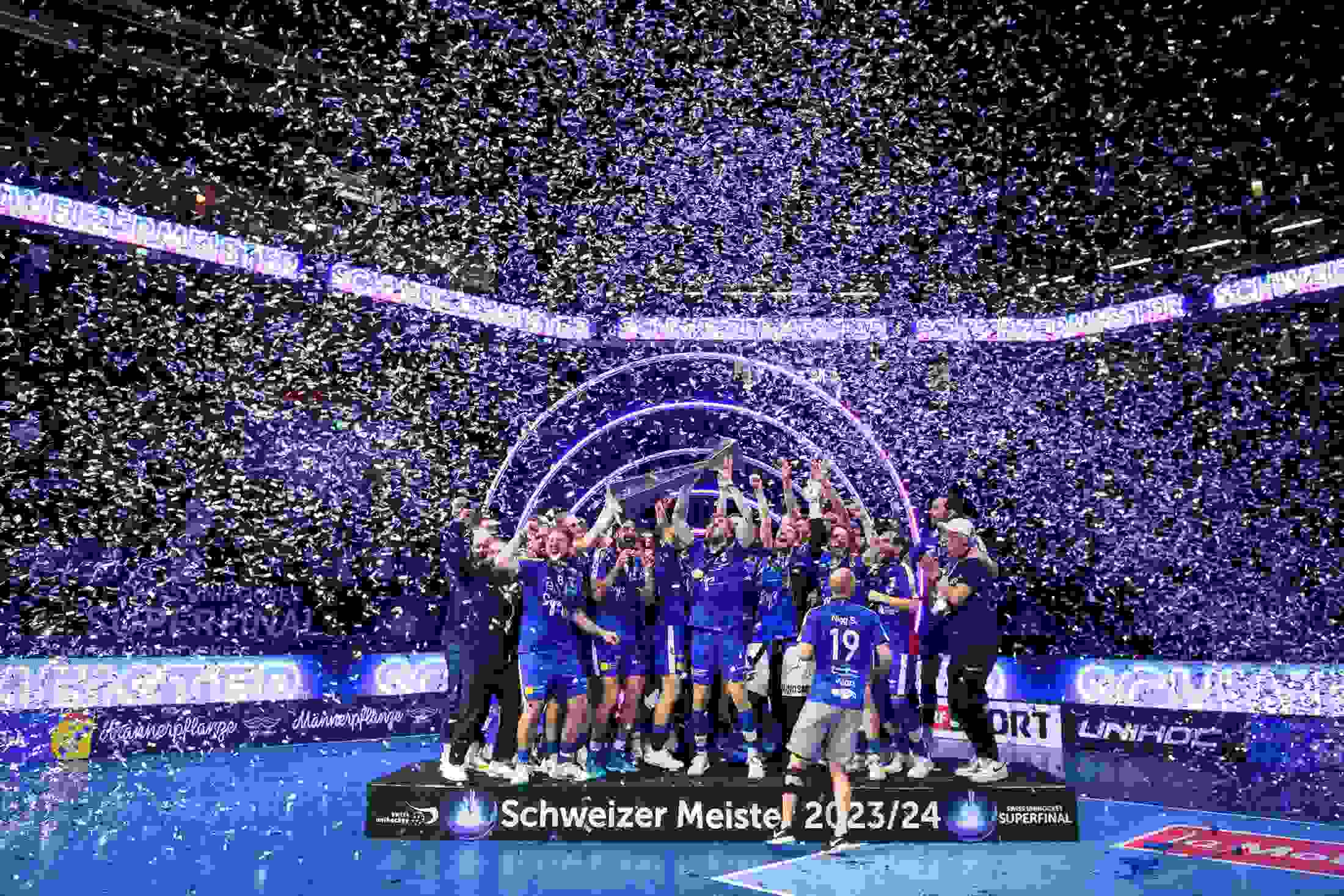 Jubelnder Unihockey-Meister mit Pokal inmitten einer Konfetti-Dusche beim Superfinal – emotionaler Höhepunkt des Tages. live kommunikation, Corporate-Event, Eventagentur bern, eventplanung, firmenevents, teamevents bern, jubiläumsfeier, networking anlass, mitarbeiteranlass, evenjo-Team, Technik, Public Events, Sport und Entertainment Events, markenerlebnis, Brand Experience, Corporate-Event, Pokal, Gewinner Team, BCF Arena Fribourg