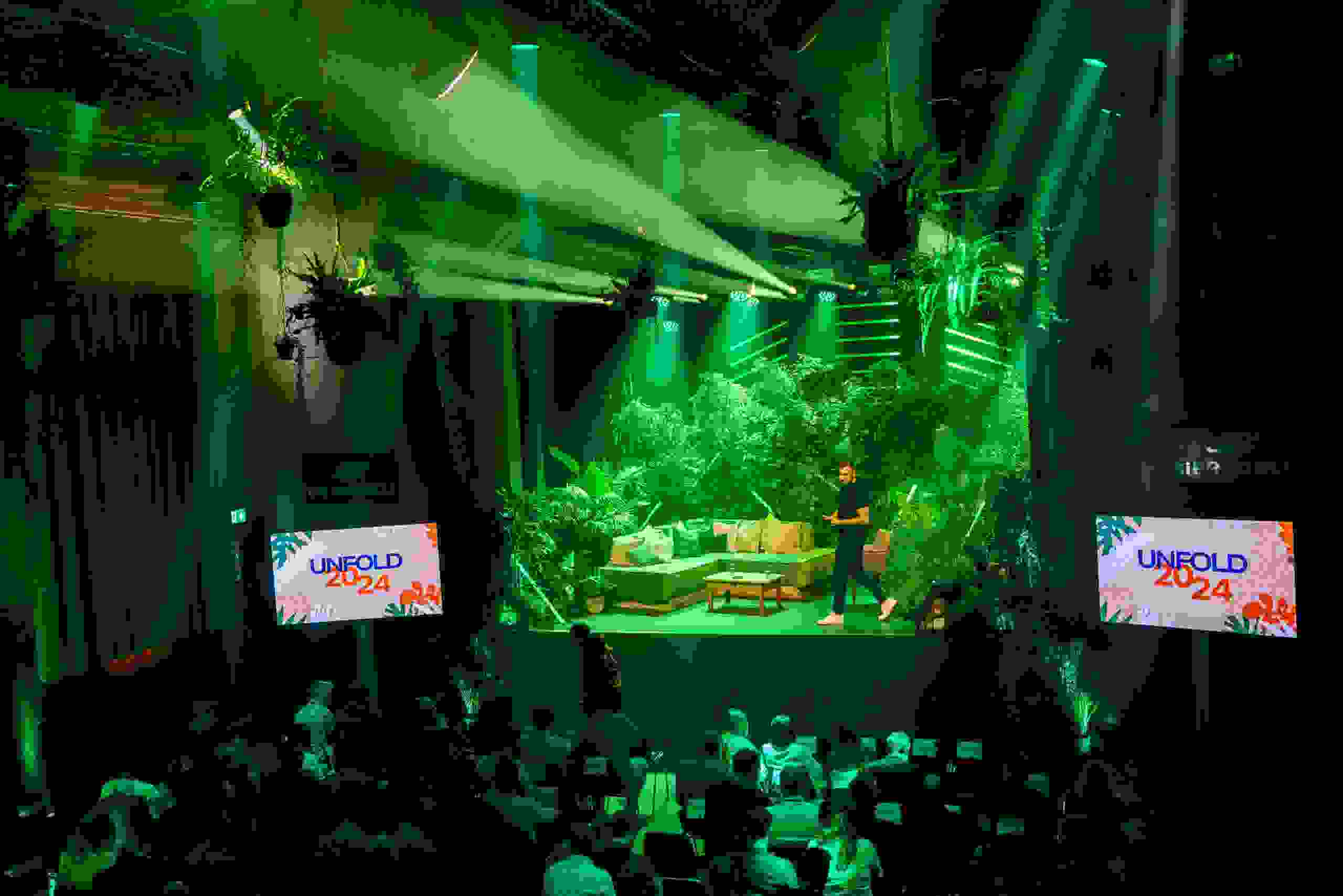 Bühnenbild im Dschungel-Look mit grünem Licht und üppiger Bepflanzung beim Corporate Event Unfold 2024 von Cleverclip im Bierhübeli Bern. Corporate Event, Eventbühne, Eventdesign, grüne Lichtstimmung, Dschungel Deko, Business Event, live kommunikation, Eventagentur bern, eventplanung, firmenevents, teamevents bern, jubiläumsfeier, networking anlass, mitarbeiter:innenanlass, Technik, Public Events, Sport und Entertainment Events, markenerlebnis, Brand Experience