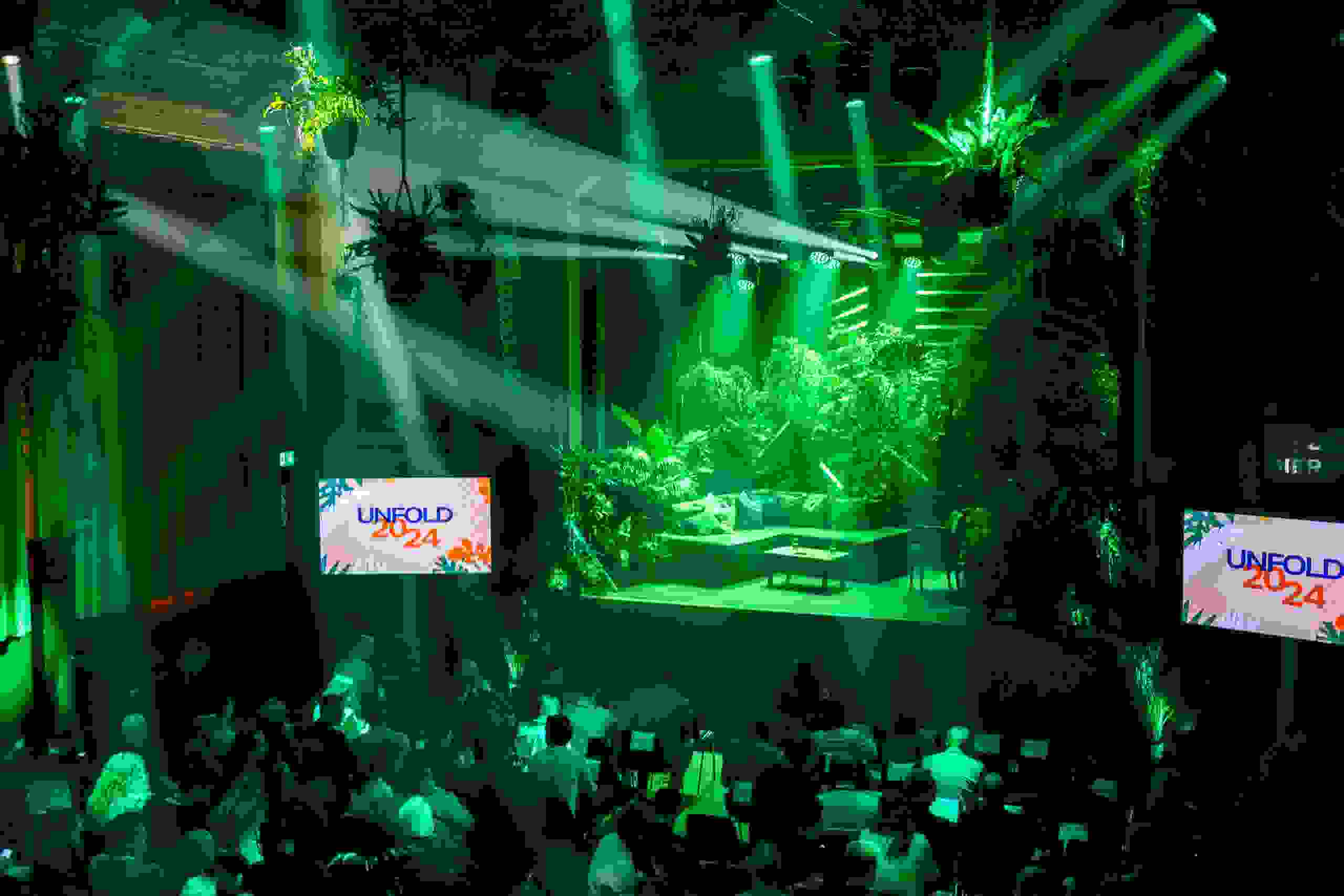Bühnenbild im Dschungel-Look mit grünem Licht und üppiger Bepflanzung beim Corporate Event Unfold 2024 von Cleverclip im Bierhübeli Bern. Corporate Event, Eventbühne, Eventdesign, Bierhübeli Bern, grüne Lichtstimmung, Dschungel Deko, Business Event, Eventagentur Schweiz, live kommunikation, Eventagentur bern, eventplanung, firmenevents, teamevents bern, jubiläumsfeier, networking anlass, mitarbeiter:innenanlass, Technik, Public Events, Sport und Entertainment Events, markenerlebnis, Brand Experience