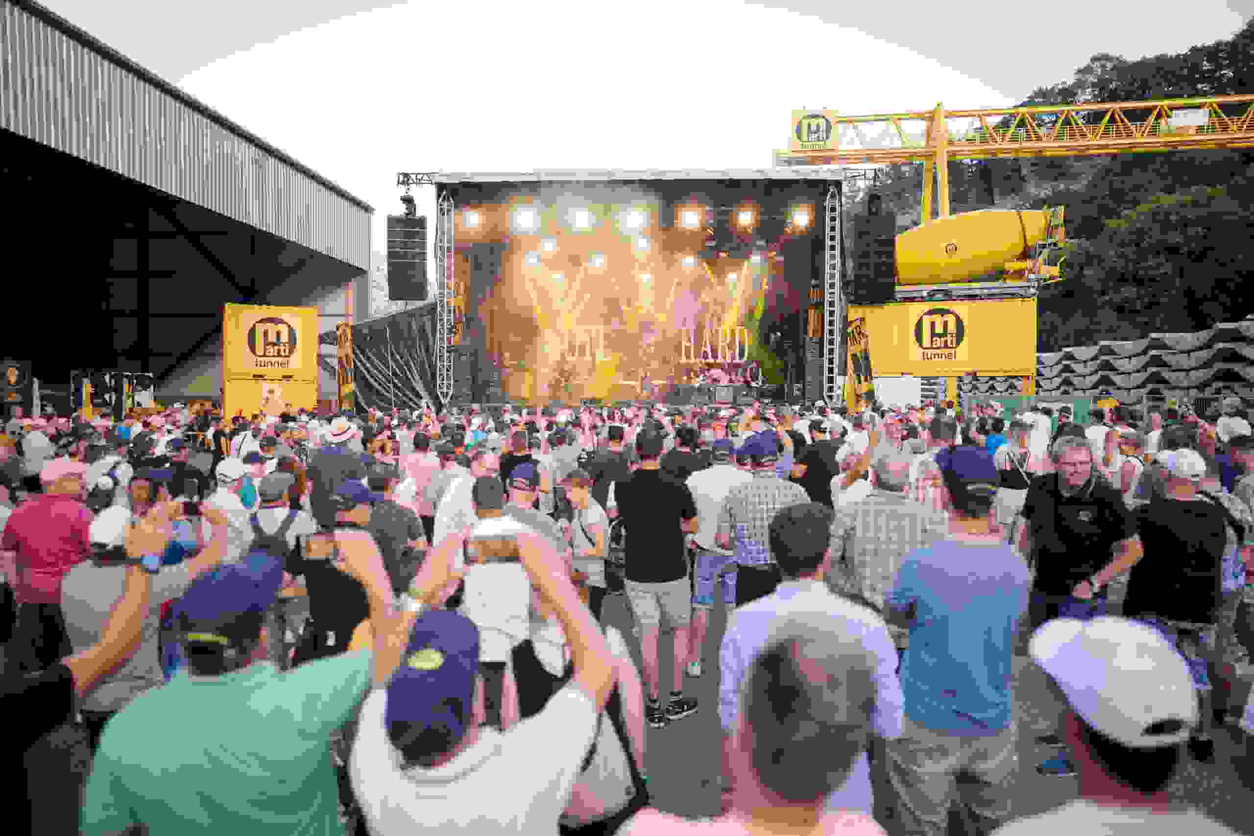 Besucher:innen feiern vor der grossen Bühne beim Konzert der Band Gotthard am Marti United 100 Jubiläumsevent. Marti United 100, Konzert, Gotthard, Live-Musik, Firmenjubiläum, Eventstimmung, Open-Air-Bühne, Bauindustrie-Event, Markenerlebnis, Brand Experience, Mitarbeiteranlass, Live Kommunikation, Corporate-Event 