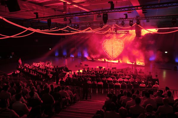 Bühnen-Show mit roter Lichtinszenierung und grossem LED-Herz-Visual beim Mobiliar Avanti Event. Live-Kommunikation, Eventtechnik, Bühnenshow, Markenerlebnis, Brand Experience, Eventplanung, Publicevent, Eventagentur Bern, Technik, Beleuchtung, Live Kommunikation, networking anlass, Mitarbeiteranlass, Mitarbeiter:innen-anlass, Jubiläumsfeier, Weihnachstfeier firma, networking anlass, Corporate-Event