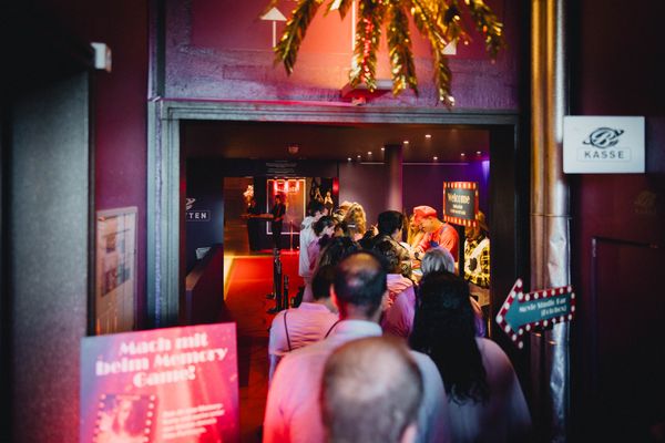 Besucher betreten die bunt beleuchtete Eventlocation mit kreativer Hollywood-Deko. Abendveranstaltung, Live-Entertainment, Eventinszenierung, Bierhübeli, Markenerlebnis, Brand Experience, Eventplanung, Publicevent, Eventagentur Bern, Technik, Live Kommunikation, networking anlass, Mitarbeiteranlass, Mitarbeiter:innen-anlass, Jubiläumsfeier, Weihnachstfeier firma, Corporate-Event