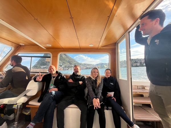 evenjo-Team auf Bootstour mit Blick auf Berge und See. Teamevent, Betriebsausflug, Markenerlebnis, Brand Experience, Eventplanung, Publicevent, Eventagentur Bern, Corporate-Event, Mitarbeiteranlass, Mitarbeiter:innen-Anlass, Live Kommunikation, networking Anlass, Ausflug, Teambuilding, Teamspirit