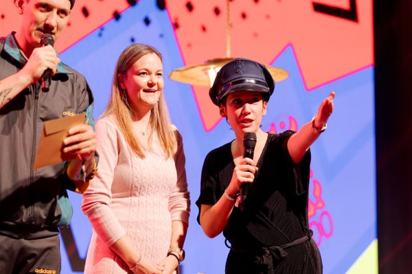 Moderatorin Gülsha Adilji mit Mikrofon und Polizei-Hut führt charmant durch das Programm – humorvolle Bühnenmoderation mit Überraschungselementen. Bühnenmoderation, Publikumsnähe, Eventhumor, Supermercado, Show, eventagentur bern