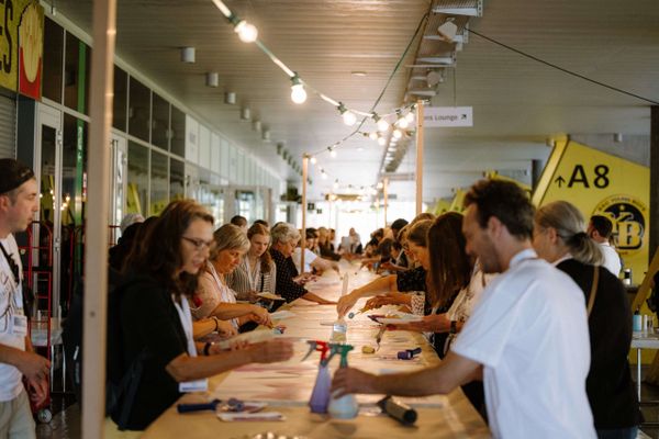 Grosse Gruppe bei einem langen Bastel- und Kreativtisch während eines Mitarbeiterevents. Teambuilding, Eventgestaltung, gemeinsames Erlebnis, Markenerlebnis, Brand Experience, Eventplanung, Publicevent, Eventagentur Bern, Technik, Live Kommunikation, networking anlass, Mitarbeiteranlass, Mitarbeiter:innen-anlass, Jubiläumsfeier, Weihnachstfeier firma, Corporate-Event