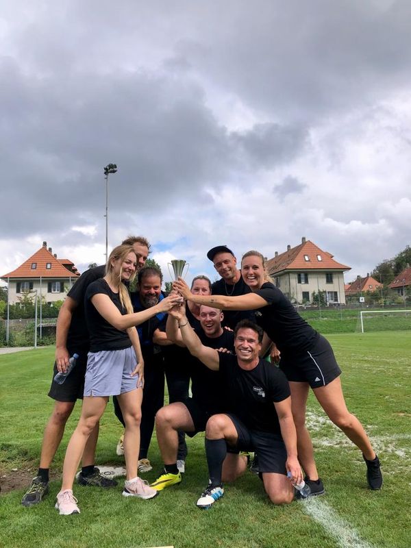 evenjo-Team jubelt mit Pokal nach Sportturnier. Teamevent, Betriebsausflug, Markenerlebnis, Brand Experience, Eventplanung, Publicevent, Eventagentur Bern, Corporate-Event, Mitarbeiteranlass, Mitarbeiter:innen-Anlass, Live Kommunikation, networking Anlass, Ausflug, Teambuilding, Sport, Sponsoring und Entertainmentment