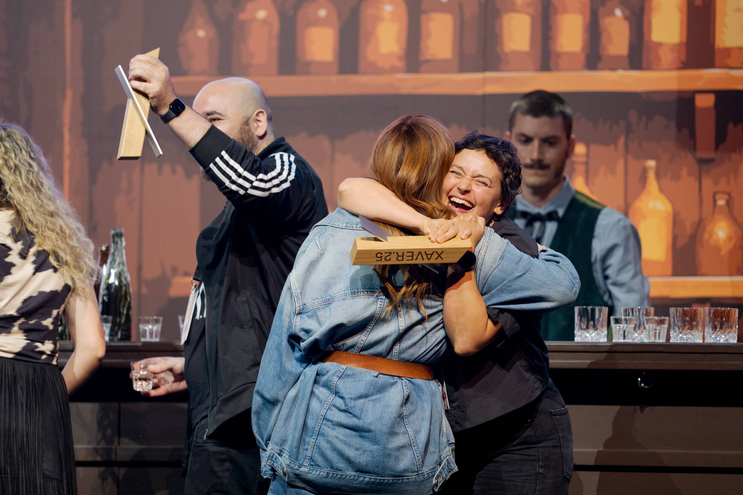 evenjo_xaveraward_preisverleihung_4.jpg Zwei Personen umarmen sich auf der Bühne der XAVER Award Show 2025, eine hält den XAVER Award in der Hand.