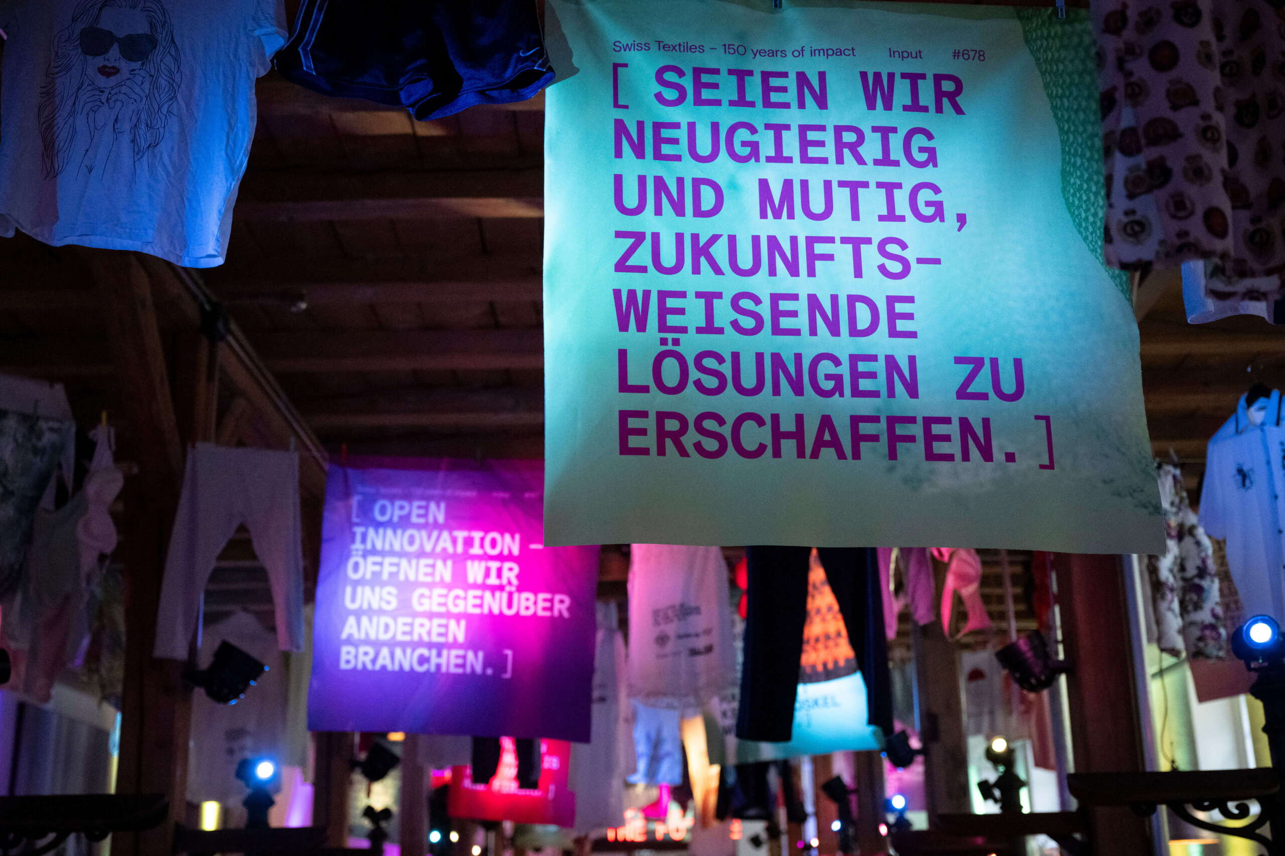 evenjo_swisstextiles_jubilaeum-67.jpg Inspirierende Statements wie „Seien wir neugierig und mutig“ auf Stoffbannern – visuelle Kommunikation für Innovationsgeist in der Textilindustrie. Innovation, Zukunftsvision, Textilbranche, Designkommunikation, Swiss Textiles 150 Jahre, reingewaschen, markenerlebnis, Brand Experience, Riithalle Zürich, Dekoration, jubiläumsfeier, mitarbeiteranlass, live kommunikation, Zukunftsorientiert, neu
