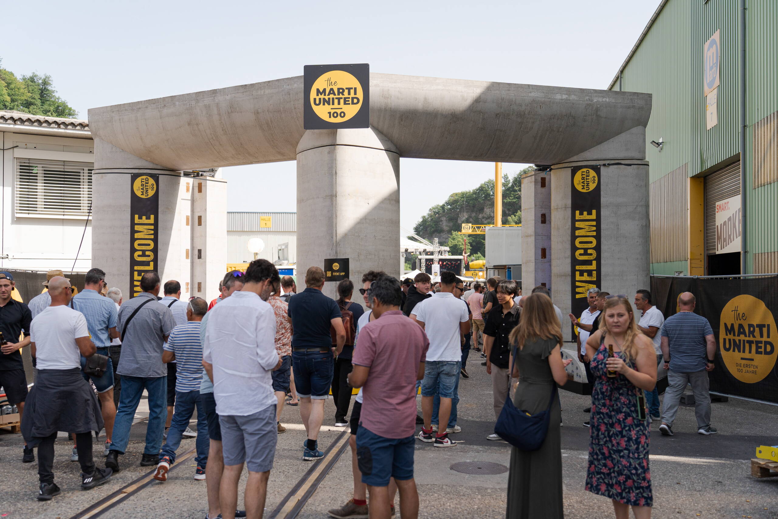 crossmediale-kommunikation-jubilaeum-marti-ag-3.jpg Besucherinnen und Besucher beim Marti United 100 Jubiläumsfest unter grossem Eingangsportal. Networking, Live-Kommunikation, Firmenjubiläum Markenerlebnis, Brand Experience, Mitarbeiteranlass, Live Kommunikation, Corporate-Event, eventplanung, Jubiläumsfeier, Mitarbeiteranlass, Teamevent, 100 Jahre Marti AG, Festival