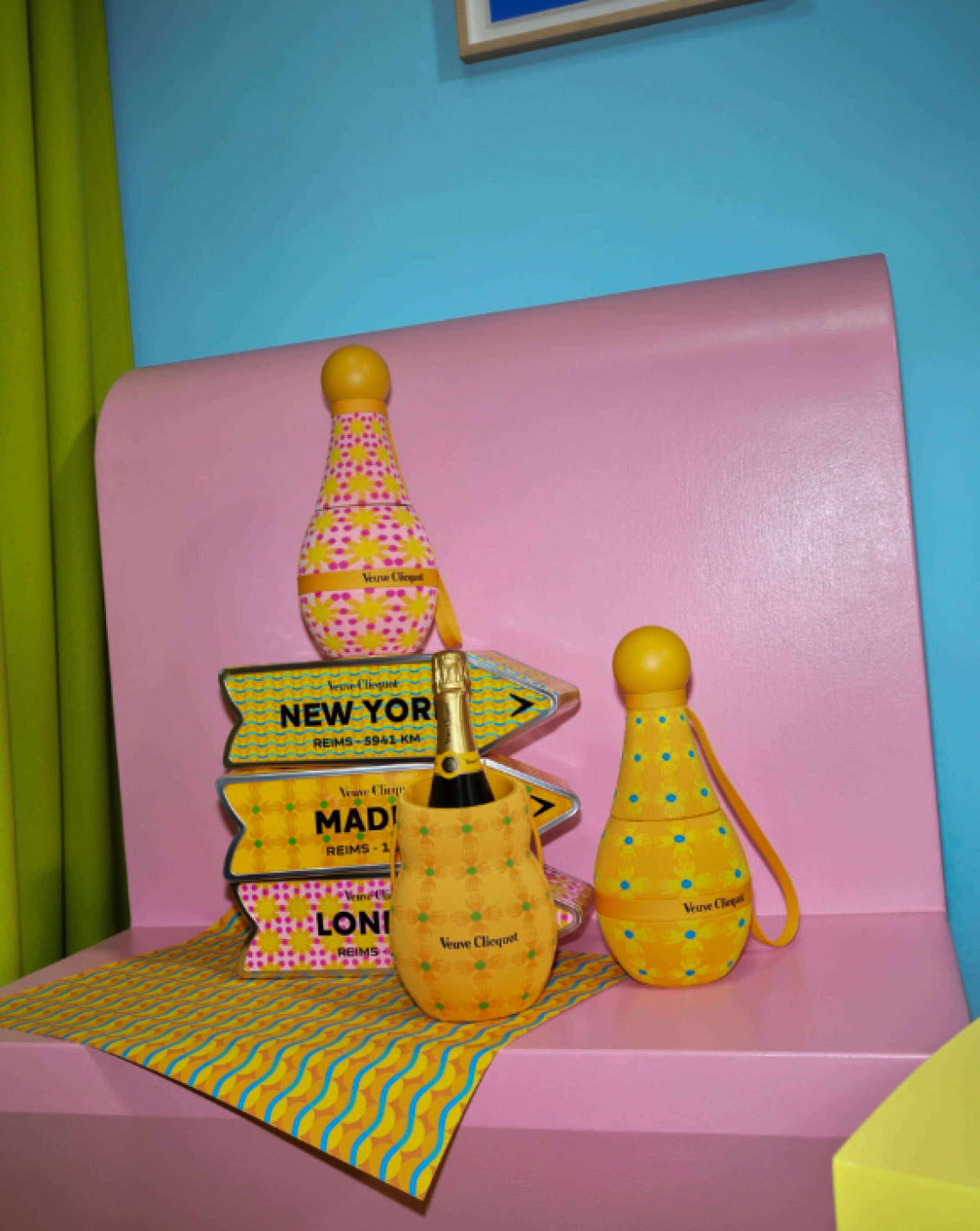 Farbenfrohe Objekte von Veuve Clicquot stehen in der Installation «Chasing the Sun» am Fuorisalone Milano auf einer rosa Sitzbank. Gelbe und pinke Muster, verspielte Wegweiser und Champagner-Accessoires erzeugen eine sommerliche, popartige Atmosphäre.