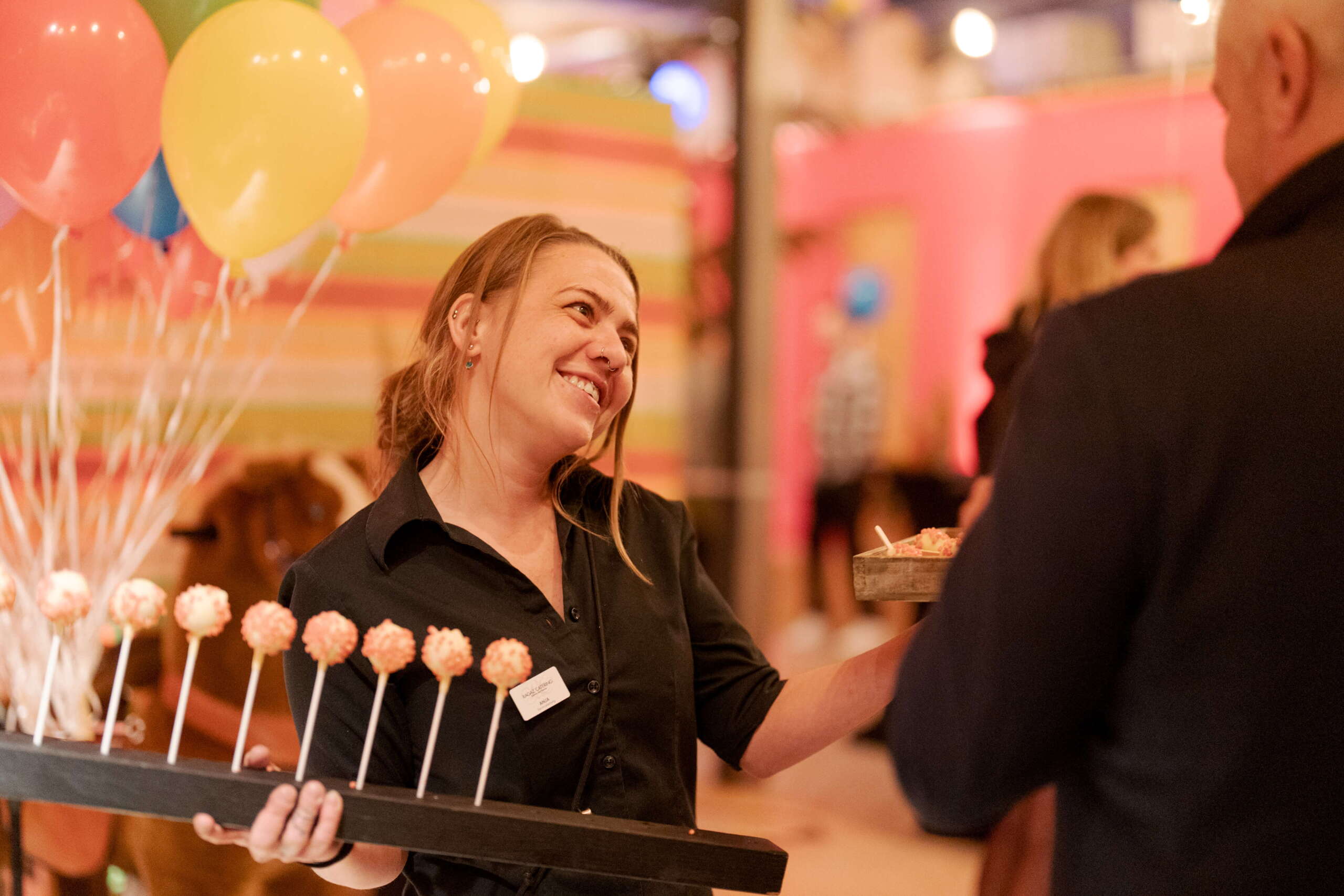 evenjo-begegnung-live-kommunikation.jpg Lachende Servicekraft mit Cake Pops im Gespräch bei der evenjo Sause. Begegnung, Networking, Live-Kommunikation, Eventgestaltung, Markenerlebnis, Brand Experience, Eventplanung, Publicevent, Eventagentur Bern, Corporate-Event, Mitarbeiteranlass, Mitarbeiter:innen-Anlass, Live Kommunikation, networking Anlass