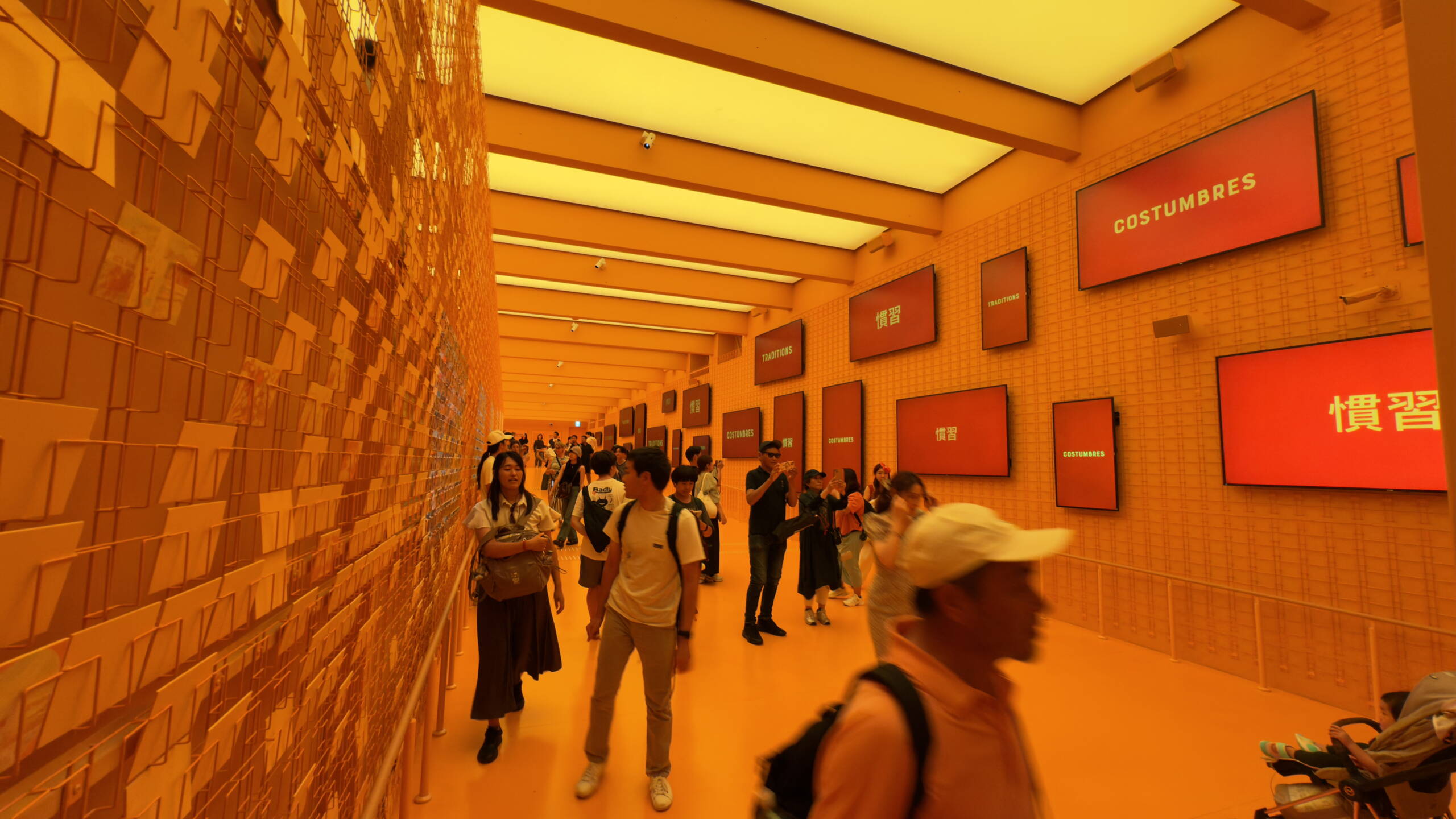 Besucher:innen bewegen sich durch einen orange beleuchteten Pavillon an der Expo Osaka mit digitalen Screens zu kulturellen Themen
