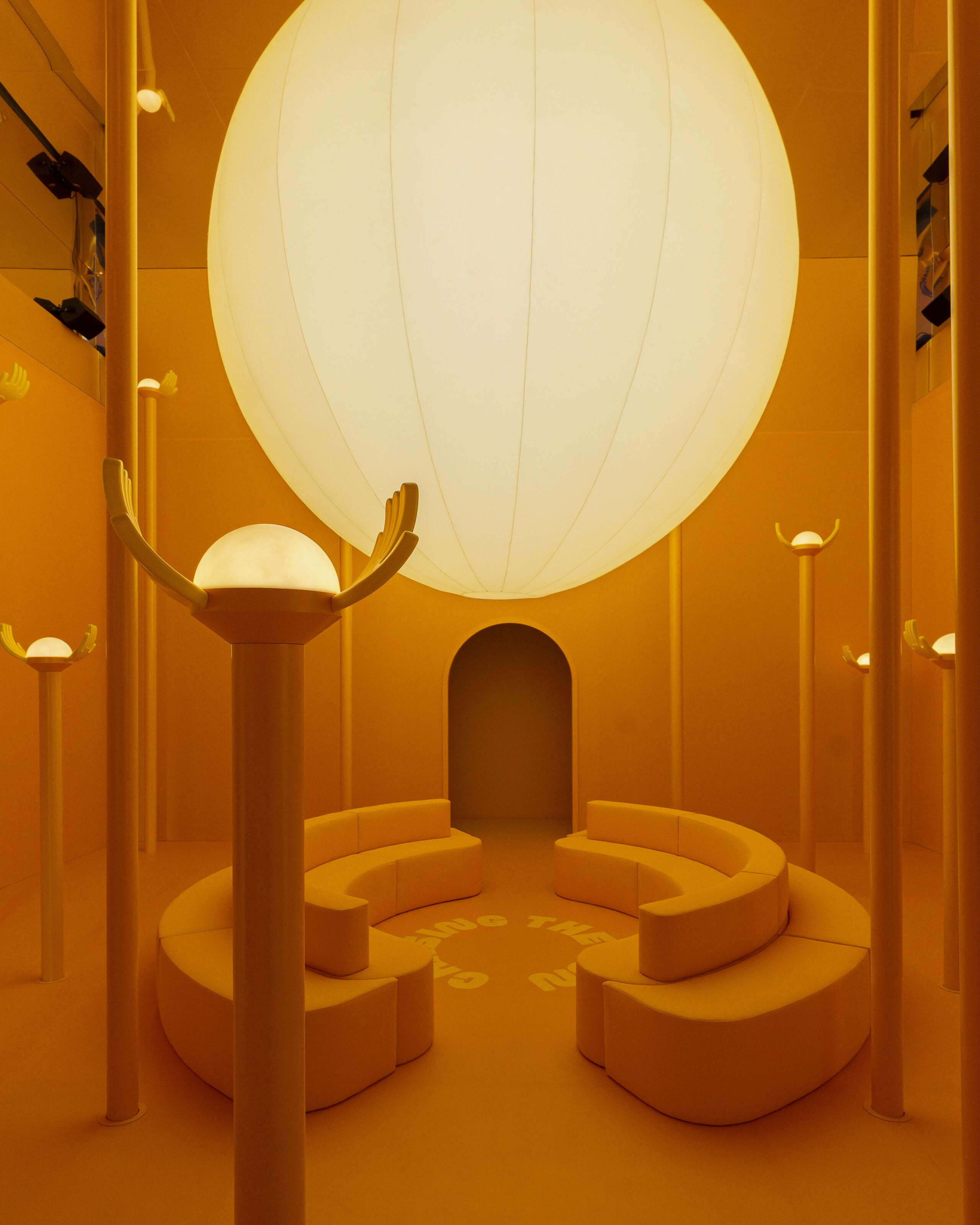Die Installation «Chasing the Sun» am Fuorisalone der Milan Design Week in Milano zeigt einen monochromen Raum in warmem Gelb und Orange. Unter einer grossen leuchtenden Kugel stehen geschwungene Sitzbänke und hohe Lichtobjekte, die an stilisierte Sonnen erinnern.