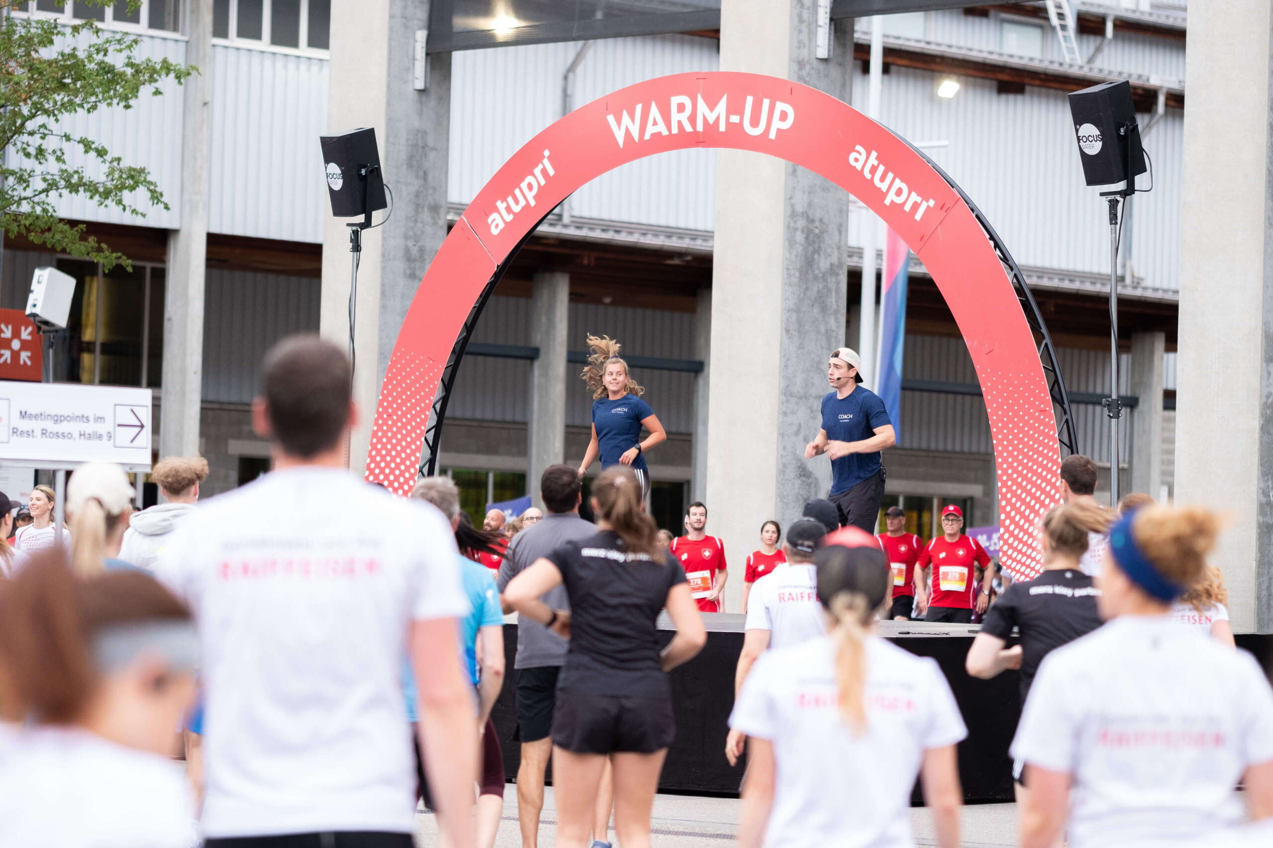 evenjo-ag-eventagentur-bern-atupri-healthbox-9.jpg ufwärmtraining vor grosser Teilnehmergruppe unter dem Atupri Healthbox WARM-UP Bogen bei Sportevent. Atupri Healthbox, Warm-up, Gruppenfitness, Outdoor-Event, Gesundheitsförderung, Teamwork, live kommunikation, Corporate-Event, Eventagentur bern, eventplanung, firmenevents, teamevents bern, jubiläumsfeier, networking anlass, mitarbeiteranlass, Technik, Public Events, Sport und Entertainment Events, markenerlebnis, Brand Experience