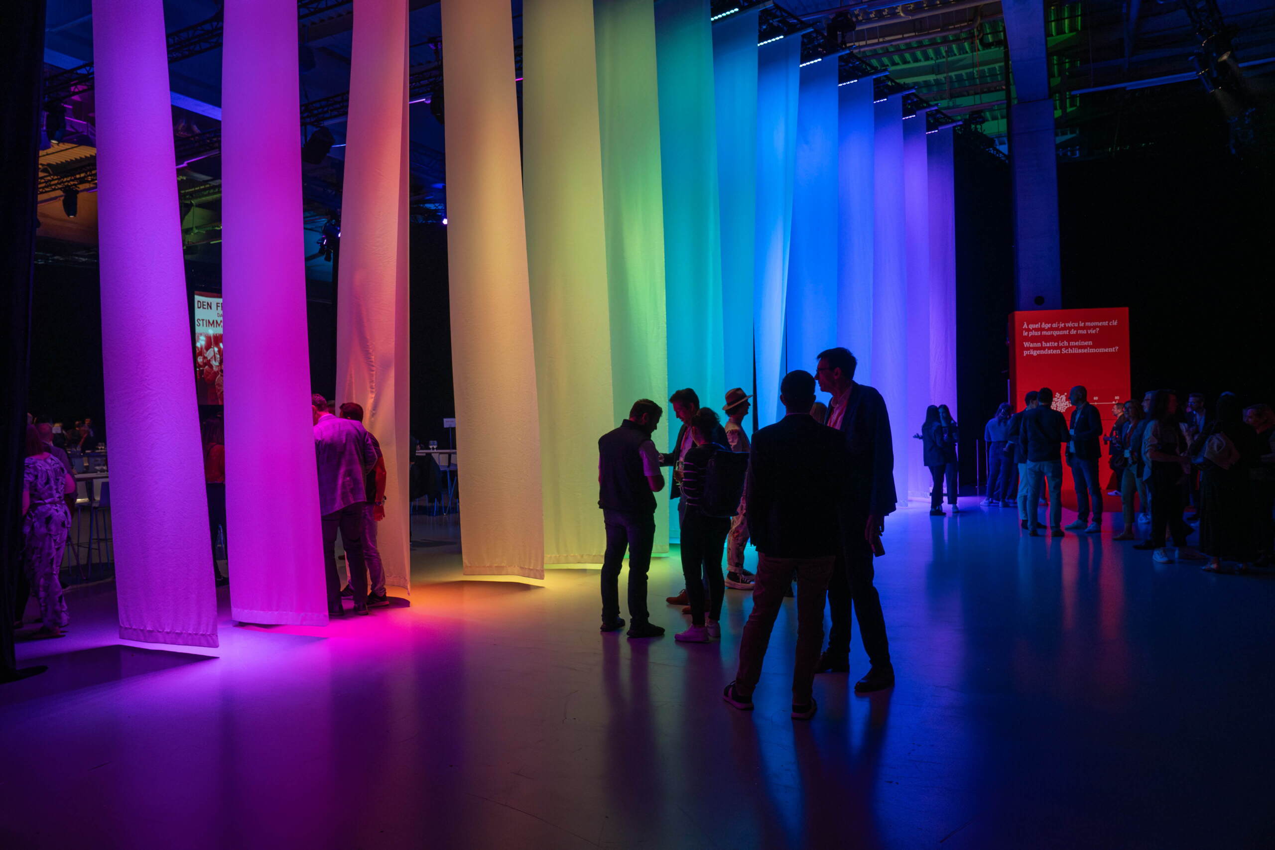 Besuchende flanieren durch bunt beleuchtete Stoffbahnen bei einem kreativen Corporate Event von Mobiliar, organisiert von evenjo. Mobiliar Event, Corporate Event, Lichtinszenierung, Brand Experience, Eventdesign, Farbinszenierung, Networking Event, live kommunikation, Corporate-Event, Eventagentur bern, eventplanung, firmenevents, teamevents bern, jubiläumsfeier, networking anlass, mitarbeiter:innenanlass