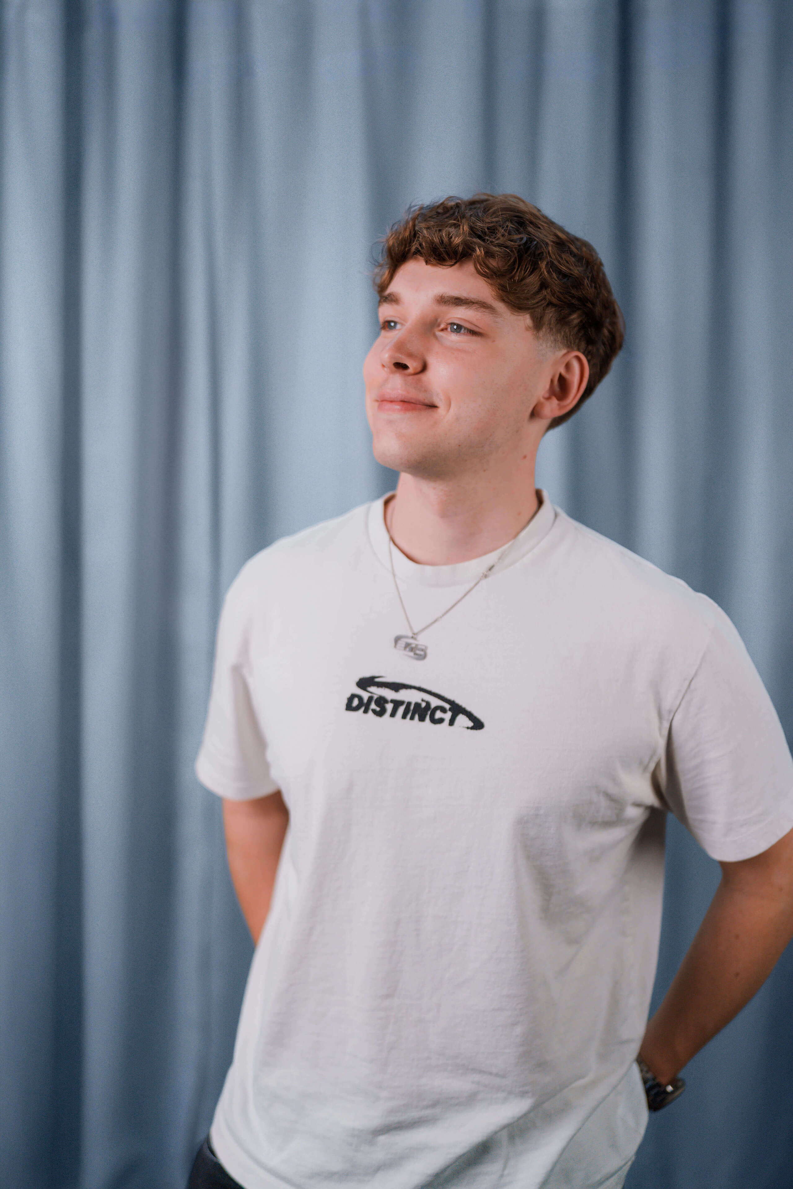 evenjo_tim_mueller_web.jpg Porträt von Tim Müller, Multimedia Producer aus dem evenjo-Team vor einem blauen Vorhang. Er trägt ein weisses T-Shirt und blickt lächelnd zur Seite.