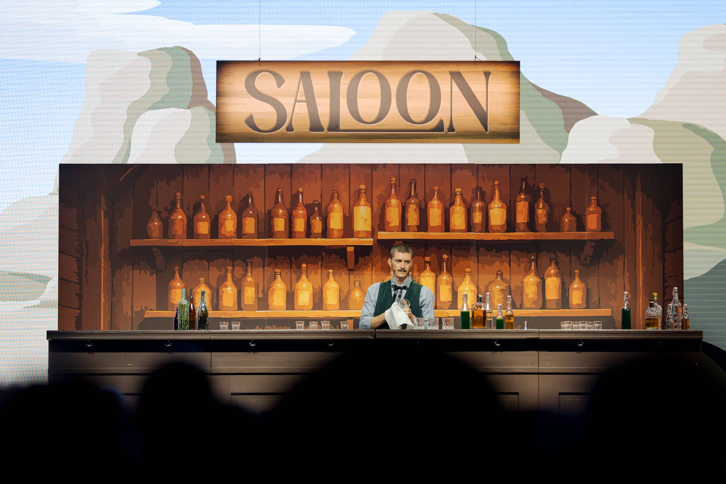 evenjo_xaveraward_preisverleihung_5.jpg Ein Barkeeper steht hinter der Western-Bar der XAVER Award Show 2025, umgeben von leuchtenden Flaschen.