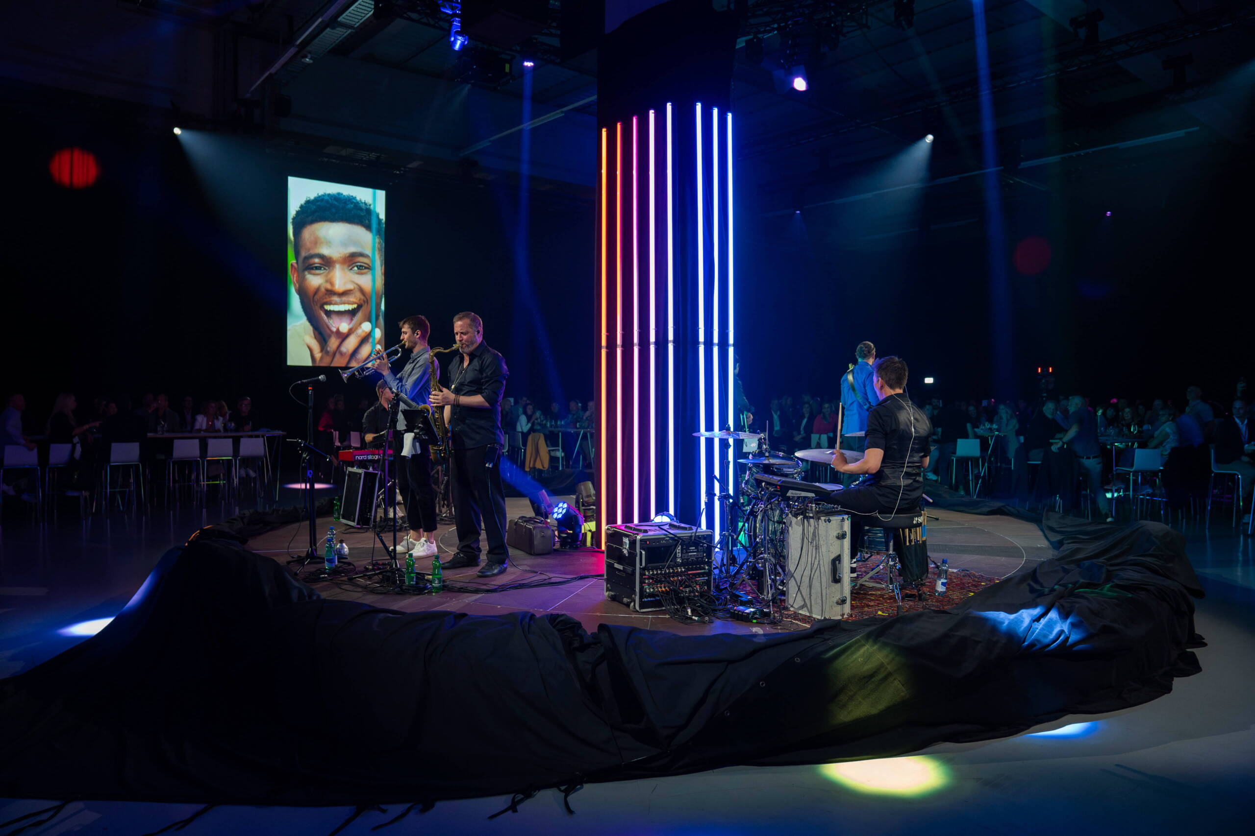 evenjo_mobiliar_avanti_corporateevent-7.jpg Liveband-Performance auf einer zentralen Eventbühne mit LED-Lichtinstallation – musikalisches Highlight und visuelles Erlebnis bei einem innovativen Corporate-Event. Liveband, Corporate Event, Eventbühne, Markenerlebnis, Eventbeleuchtung, Business Event, Brand Experience, Publikum, Leadership, Motivation, Corporate Speaker, Innovation, Markeninszenierung, eventagentur bern, markenerlebnis, Brand Experience