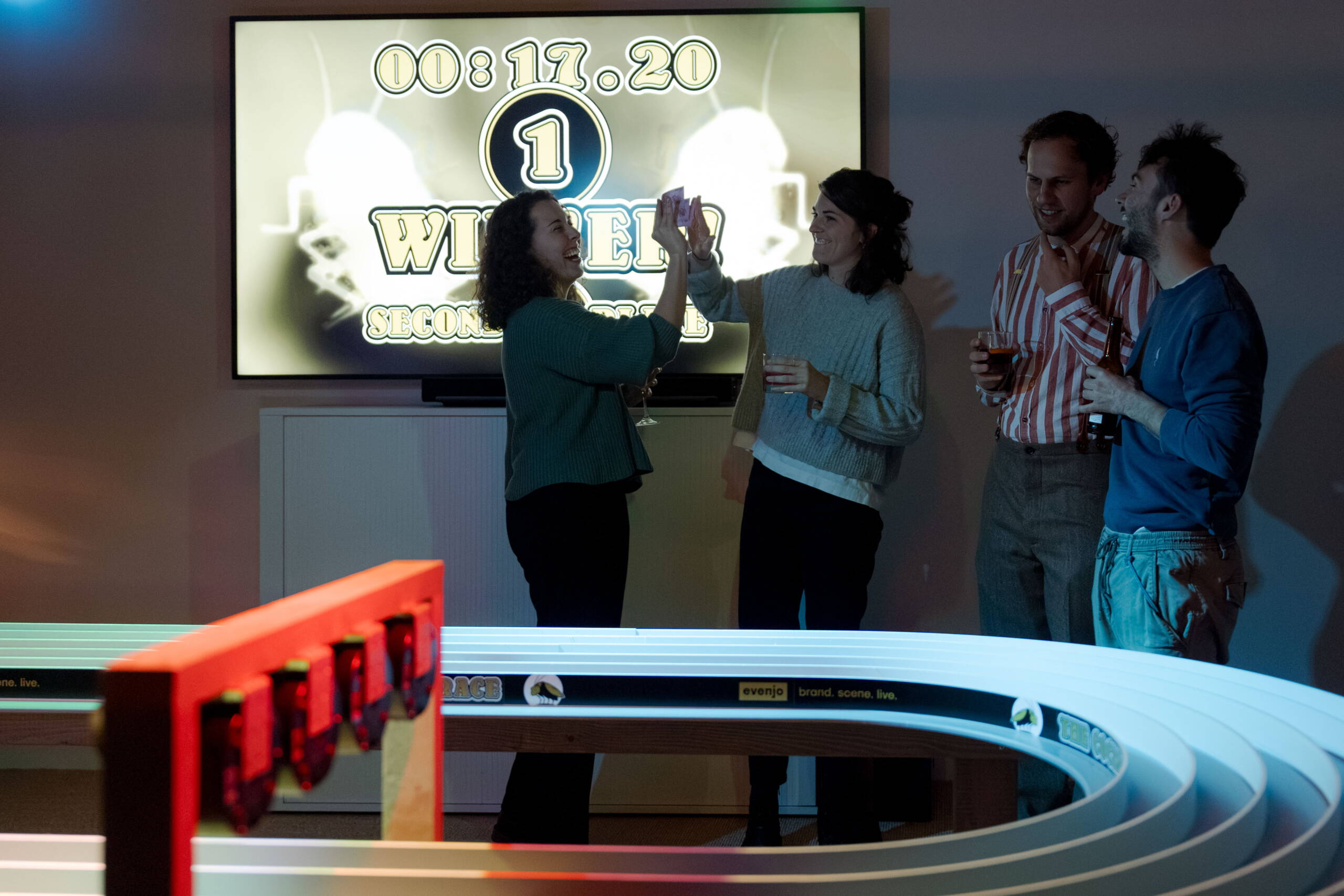 evenjo-sause-rennen.jpg Zwei Frauen feiern ihren Sieg beim Rennen mit einem High-Five vor dem Bildschirm – ausgelassene Stimmung und Teambuilding bei der evenjo Sause. markenerlebnis, Brand Experience, mitarbeiteranlass, live kommunikation, Corporate-Event, Markenerlebnis, eventplanung, jubiläumsfeier, mitarbeiteranlass, teamevent