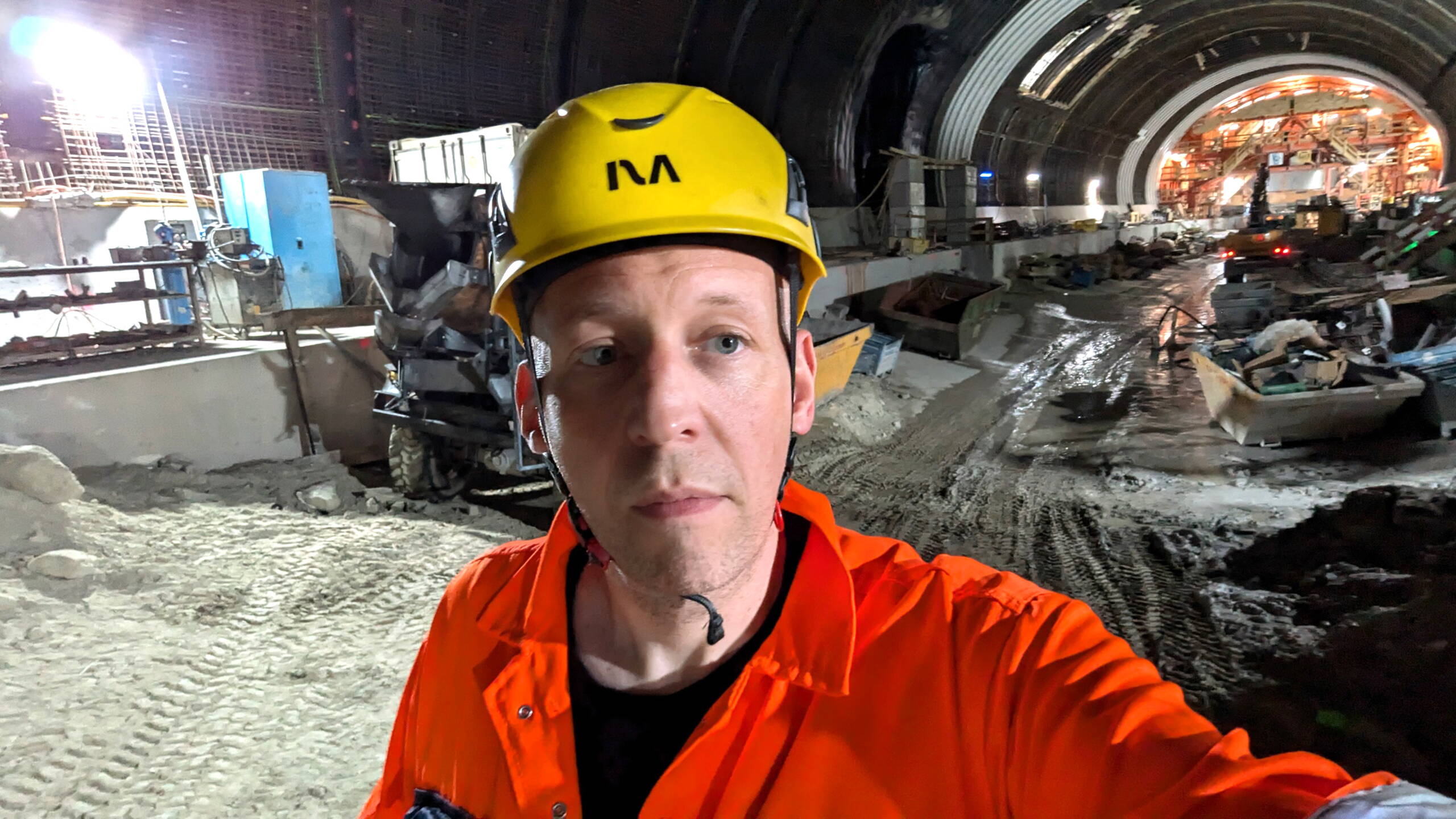 Christian Wenge, Technischer Leiter bei evenjo, in orangem Schutzanzug und gelbem Helm steht in einem Tunnel auf der Marti-Baustelle des neuen RBS-Bahnhofs Bern.