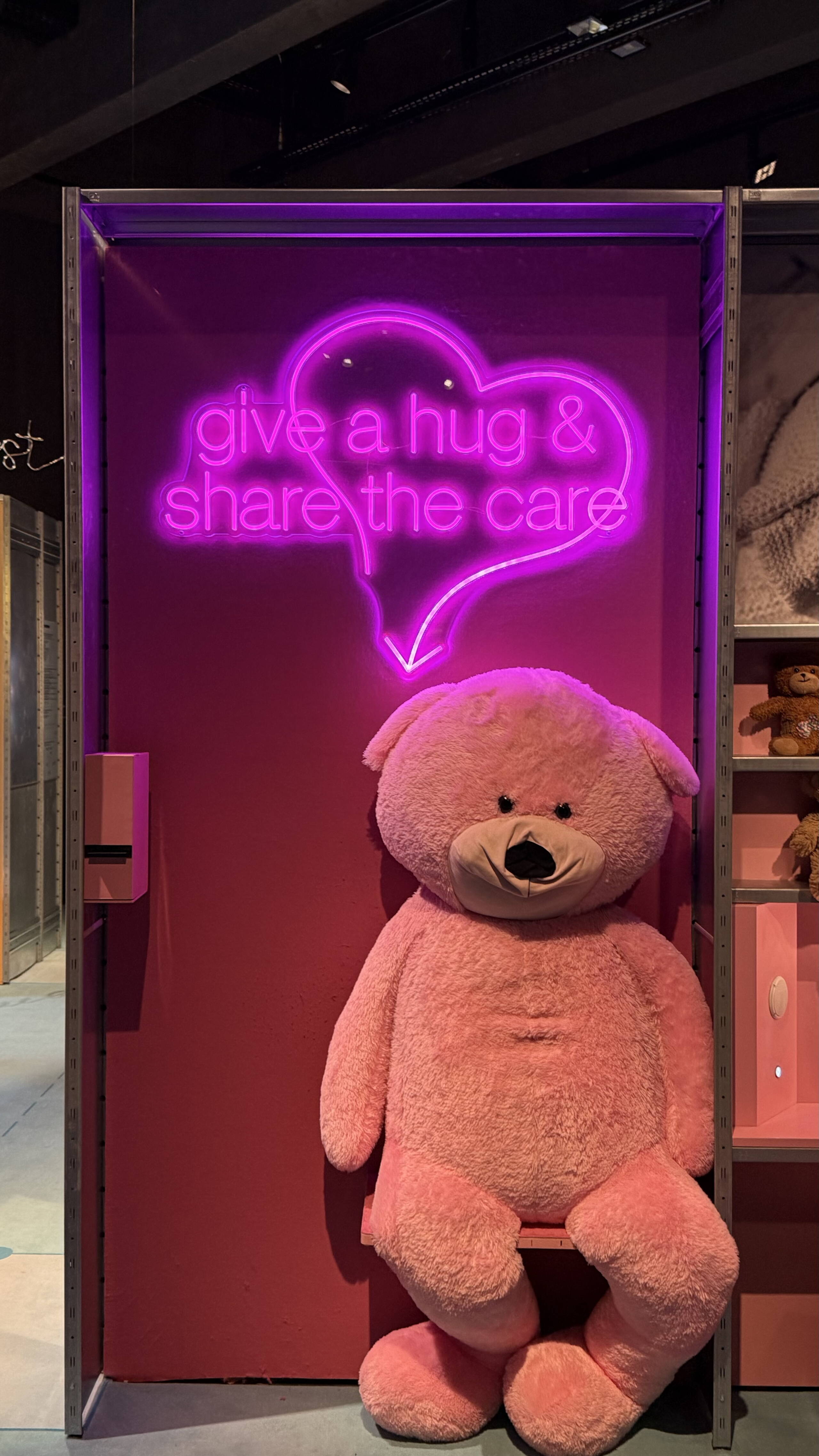 evenjo_ausstellung_stapferhaus_szenografie_inszenierung_03.jpeg Ausstellungsraum im Stapferhaus mit riesen Teddybär und pinker Neon-Leuchtschrift "give a hug & share the care". moderne Szenografie. Ausstellungsgestaltung, Inszenierung, Begegnung, Networking, Live-Kommunikation, Eventgestaltung, Markenerlebnis, Brand Experience, Eventplanung, Publicevent, Eventagentur Bern, Corporate-Event, Mitarbeiteranlass, Mitarbeiter:innen-Anlass, Live Kommunikation, networking Anlass