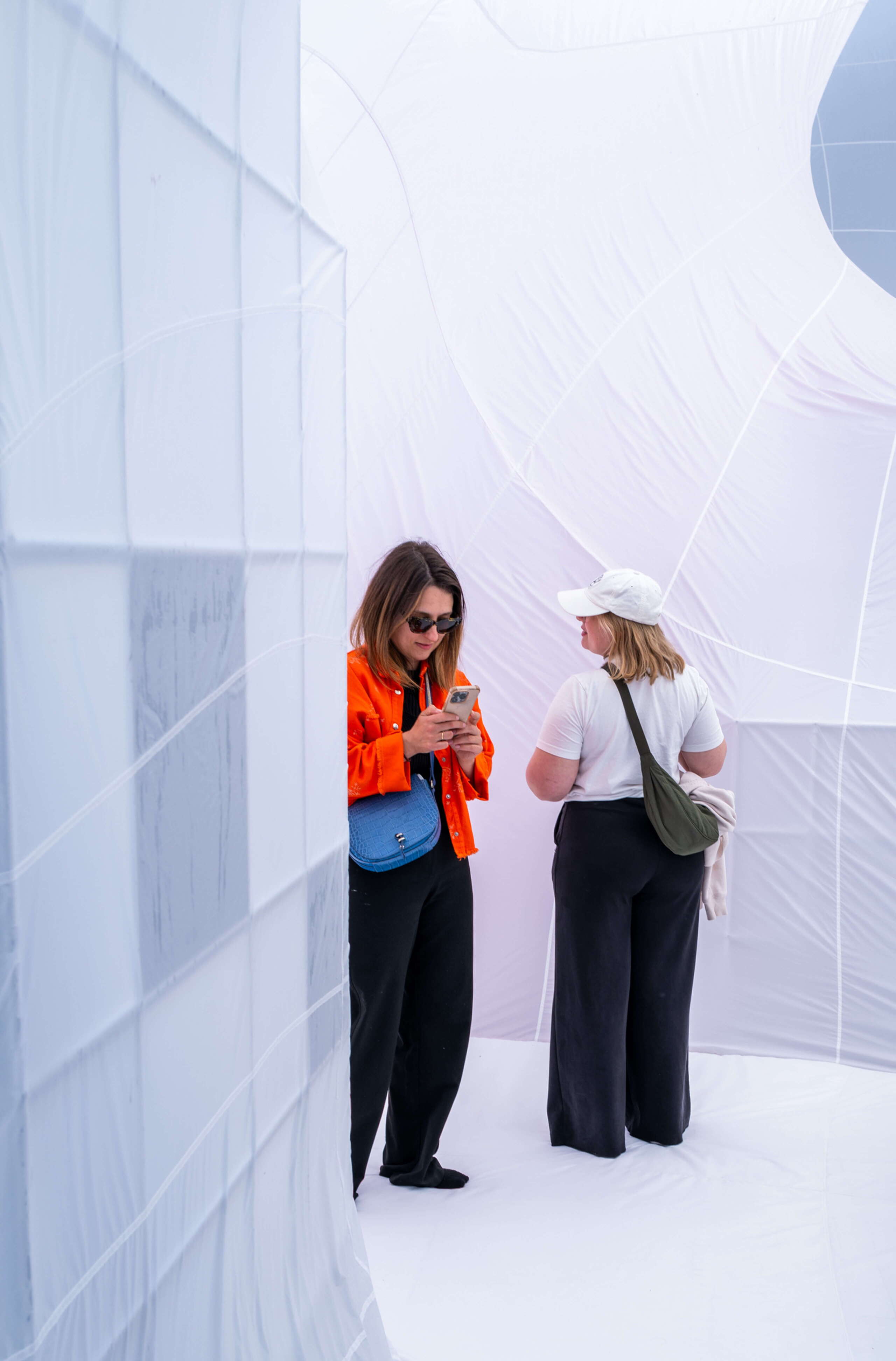 Zwei Besucherinnen stehen in der textilen USM-Installation am Fuorisalone Milano. Die weissen, geschwungenen Stoffwände und das weiche Licht erzeugen eine stille, entschleunigte Raumwirkung innerhalb der Milan Design Week.