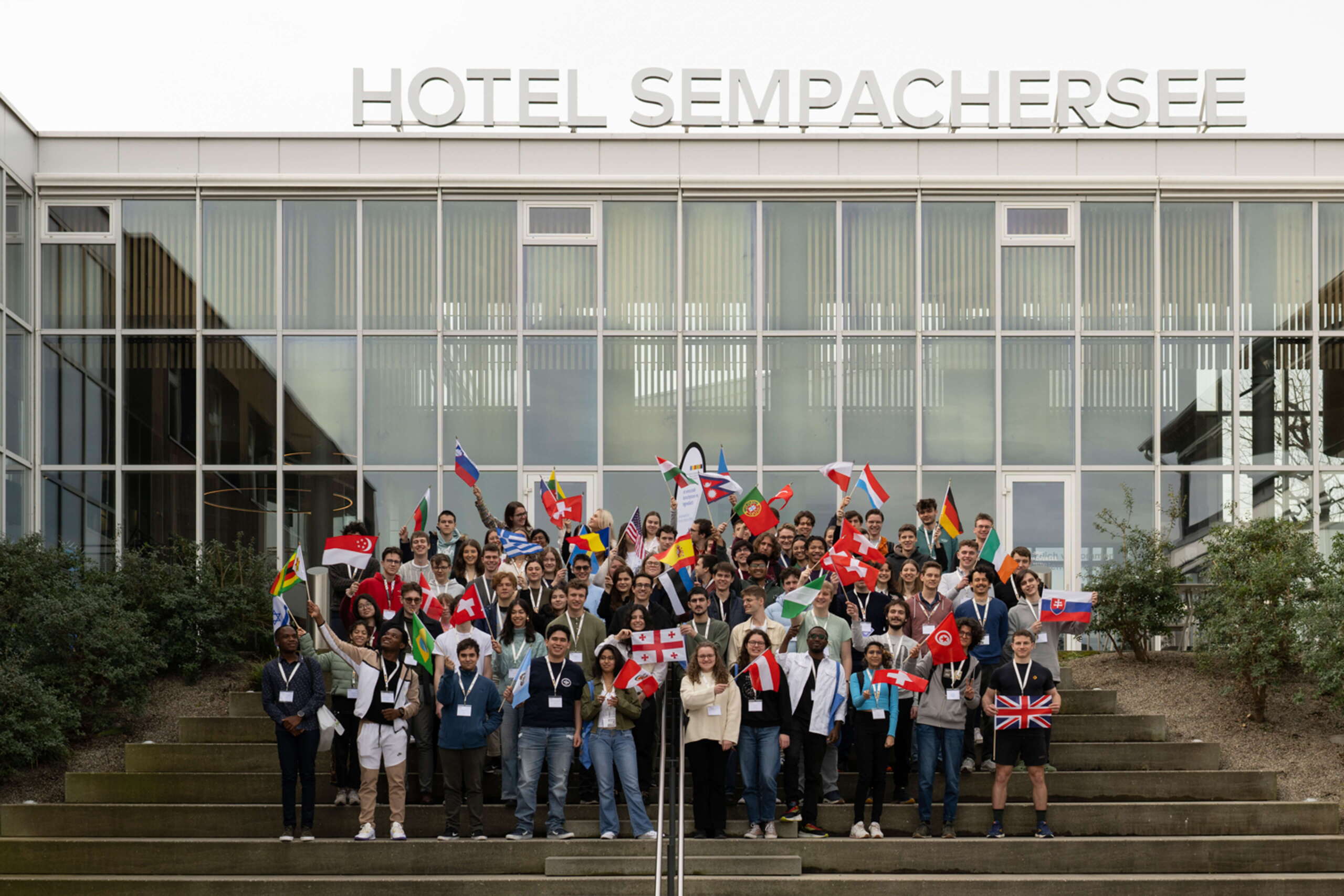 international_swiss_talent_forum_evenjo_eventagenur_bern-24.jpg Internationale Teilnehmende des Swiss Talent Forums 2024 vor dem Hotel Sempachersee mit Flaggen aus aller Welt. Gruppenfoto, Hotel Sempachersee, Flaggen, globale Teilnehmende, markenerlebnis, Brand Experience, live kommunikation, schweizer Jugend forscht
