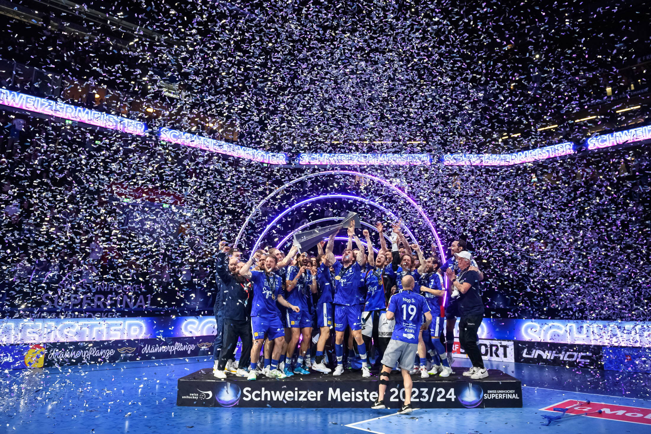evenjo_superfinal_Swiss_unihockey_sport-event_meister.jpg Jubelnder Unihockey-Meister mit Pokal inmitten einer Konfetti-Dusche beim Superfinal – emotionaler Höhepunkt des Tages. live kommunikation, Corporate-Event, Eventagentur bern, eventplanung, firmenevents, teamevents bern, jubiläumsfeier, networking anlass, mitarbeiteranlass, evenjo-Team, Technik, Public Events, Sport und Entertainment Events, markenerlebnis, Brand Experience, Corporate-Event, Pokal, Gewinner Team, BCF Arena Fribourg