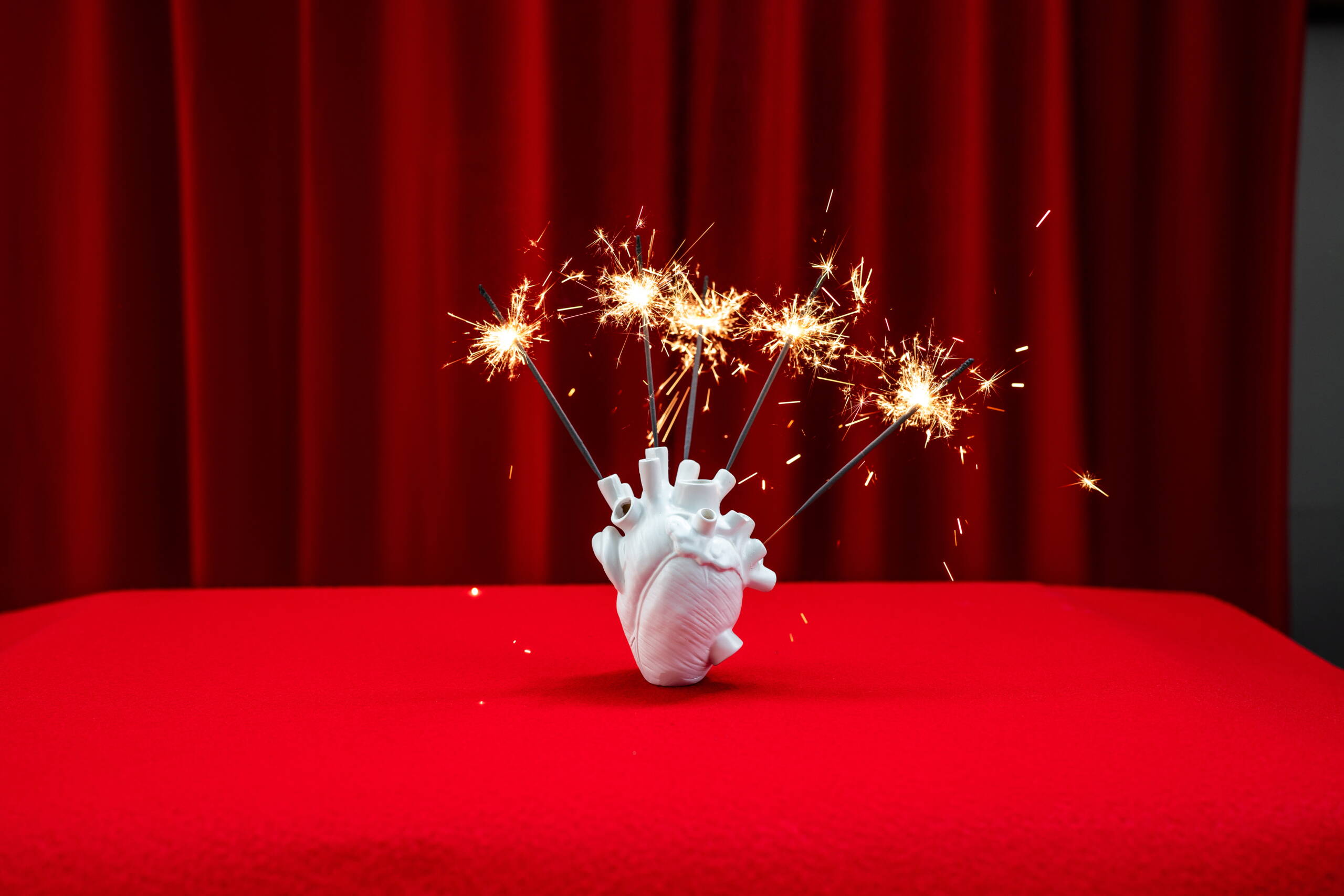 evenjo_markenerlebnisse_Herzmodell_mit_Wunderkerzen.jpg Weisses Herzmodell mit Wunderkerzen vor rotem Vorhang. Eventdesign, kreative Deko, visuelles Storytelling für Veranstaltungen, Markenerlebnis, Brand Experience, Eventplanung, Publicevent, Eventagentur Bern, Technik, Beleuchtung, Live Kommunikation